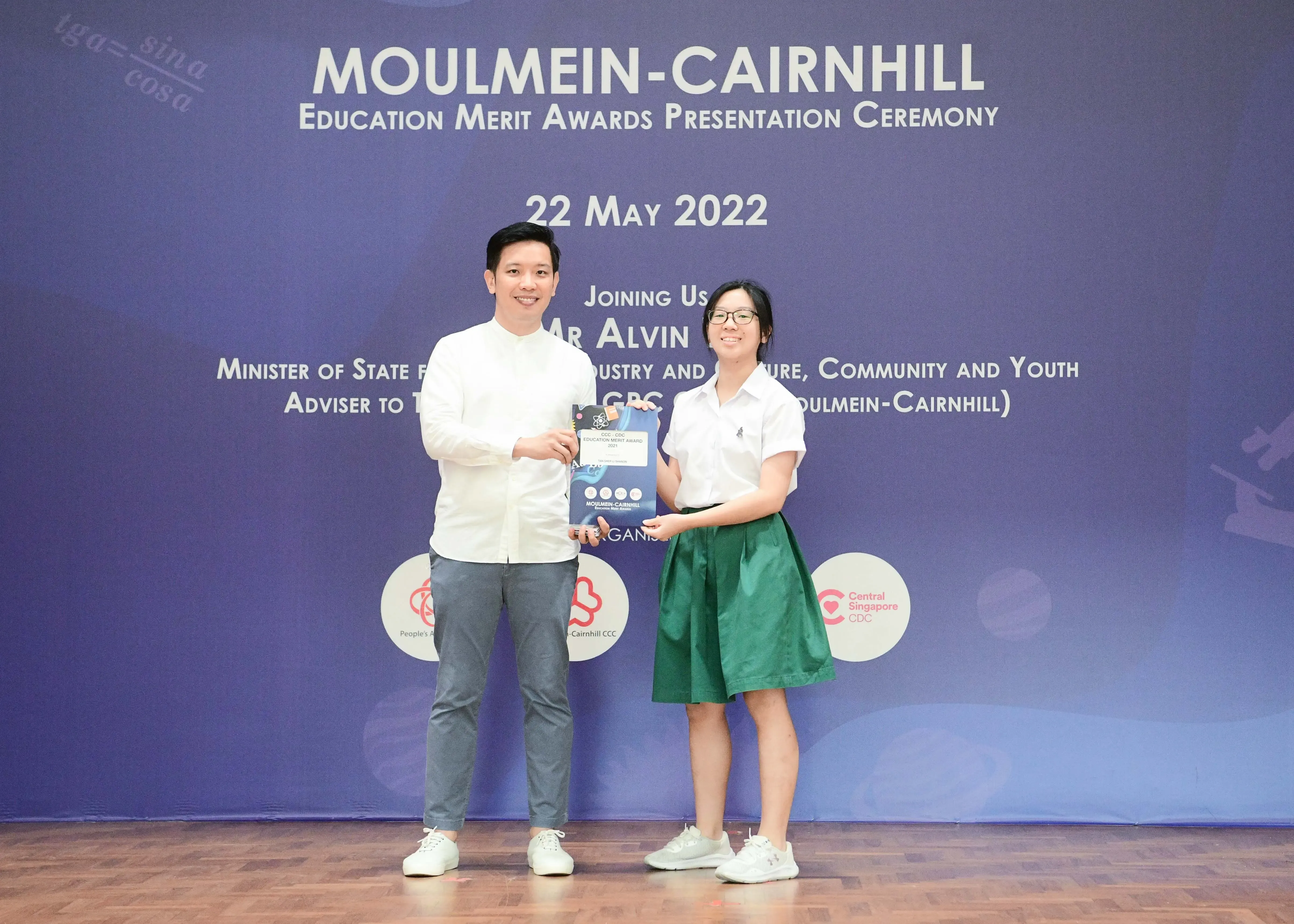 Two people hold an award booklet on stage at the Moulmein-Cairnhill Education Merit Awards Ceremony on 22 May 2022.