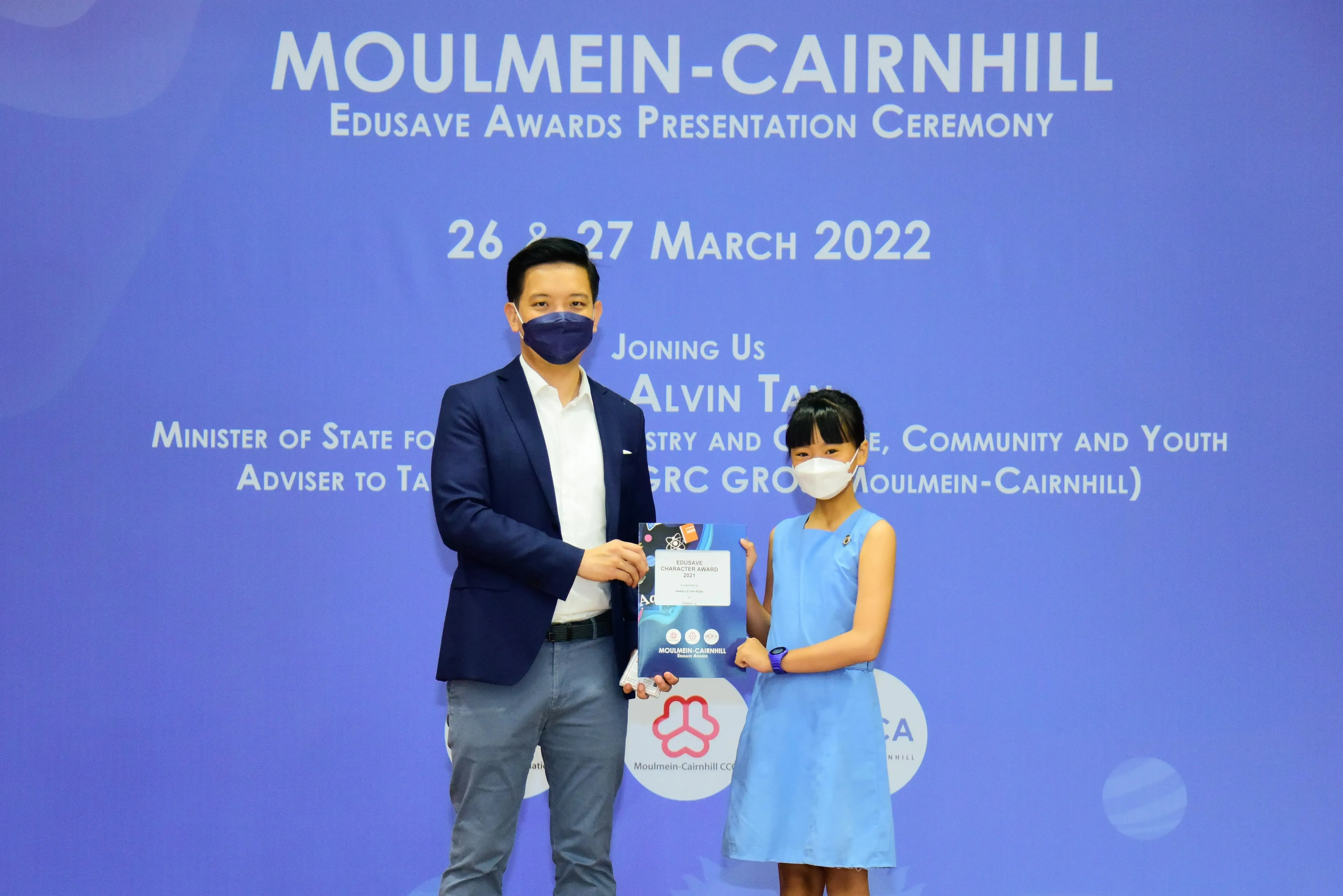 A masked man and young girl hold a certificate at the Moulmein-Cairnhill Edusave Awards Ceremony, March 2022.