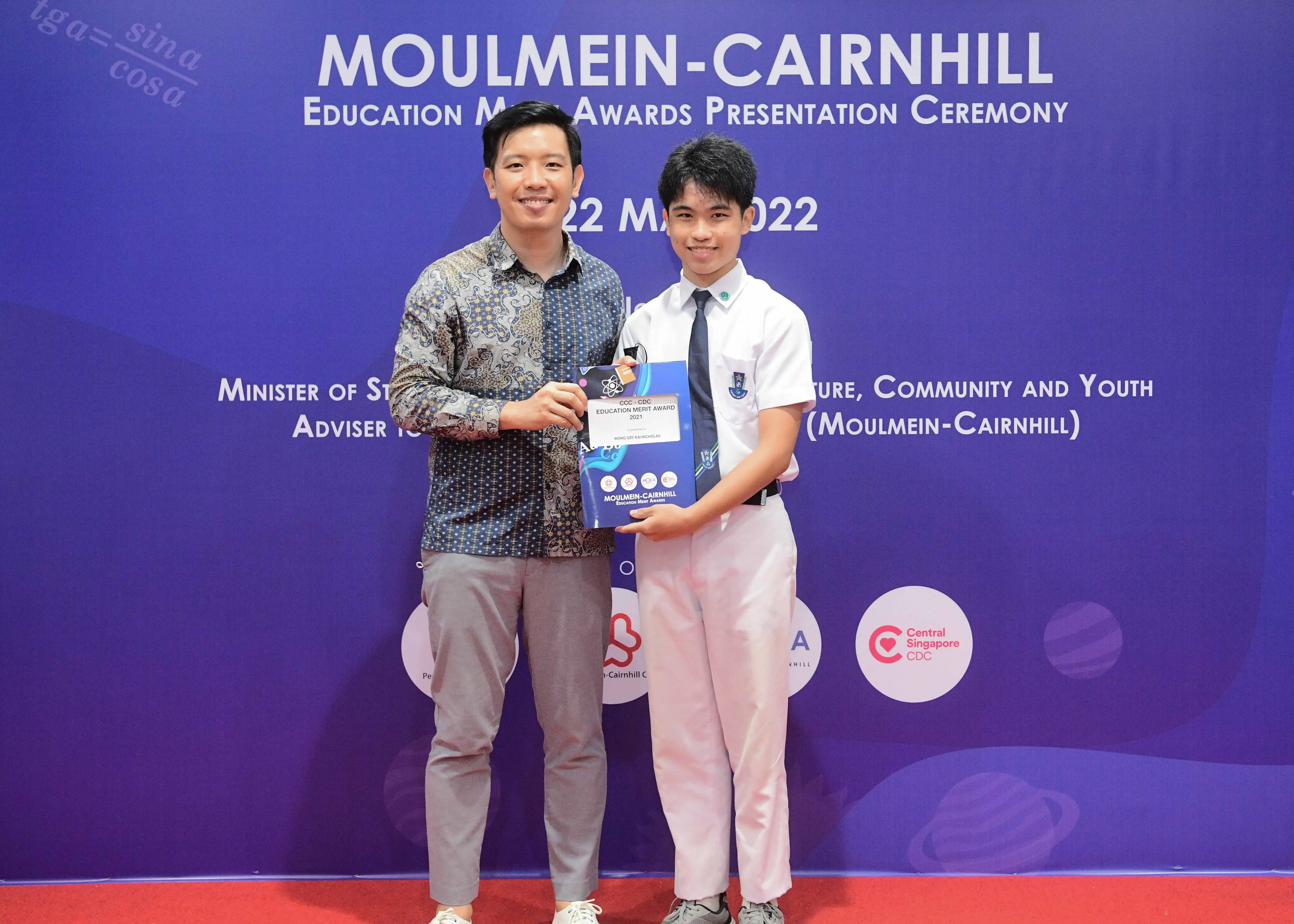 Two people pose holding an award certificate at the Moulmein-Cairnhill Education Merit Awards Ceremony on 22 May 2022.