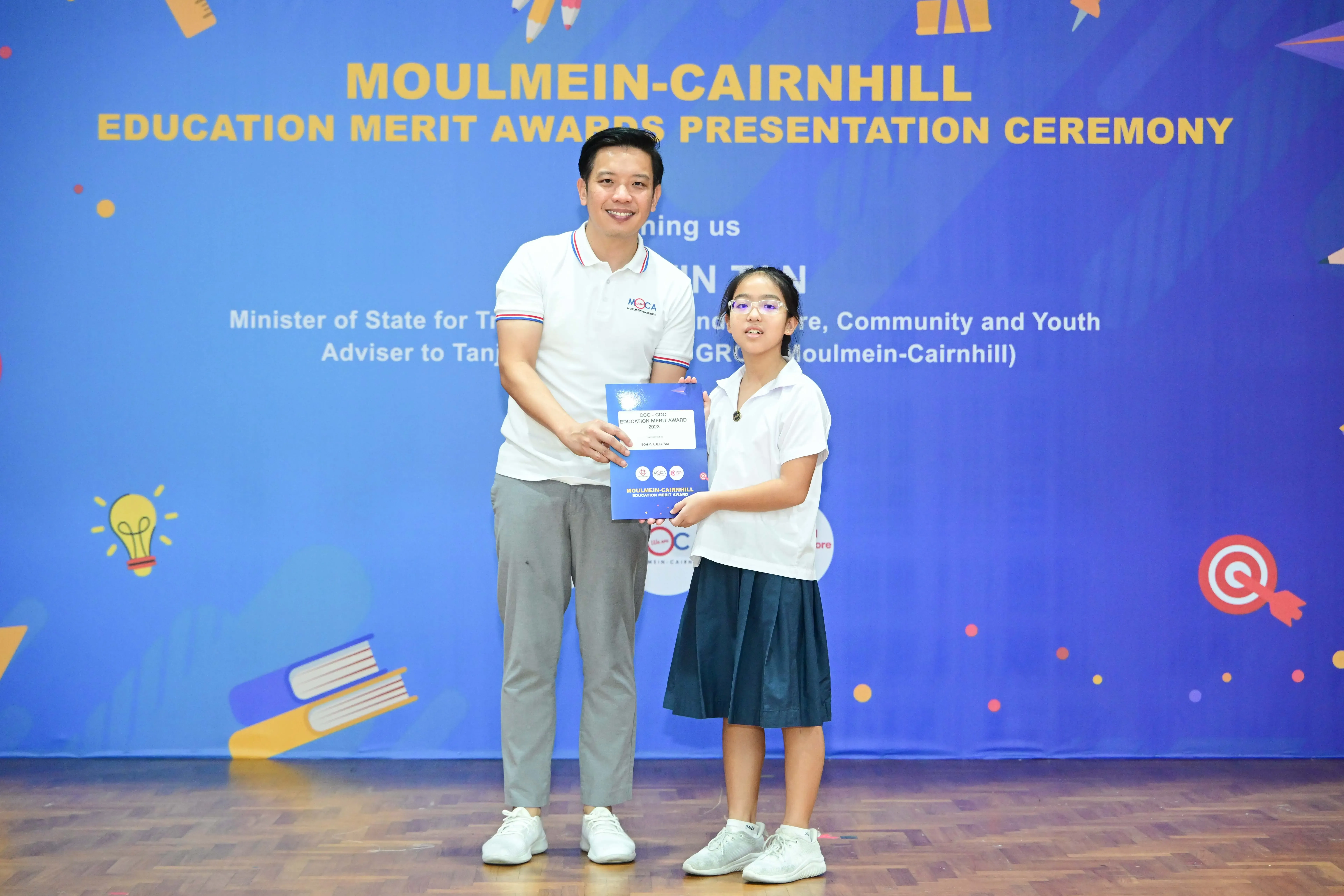 A man and a young girl hold an award certificate at the Moulmein-Cairnhill Education Merit Awards ceremony.