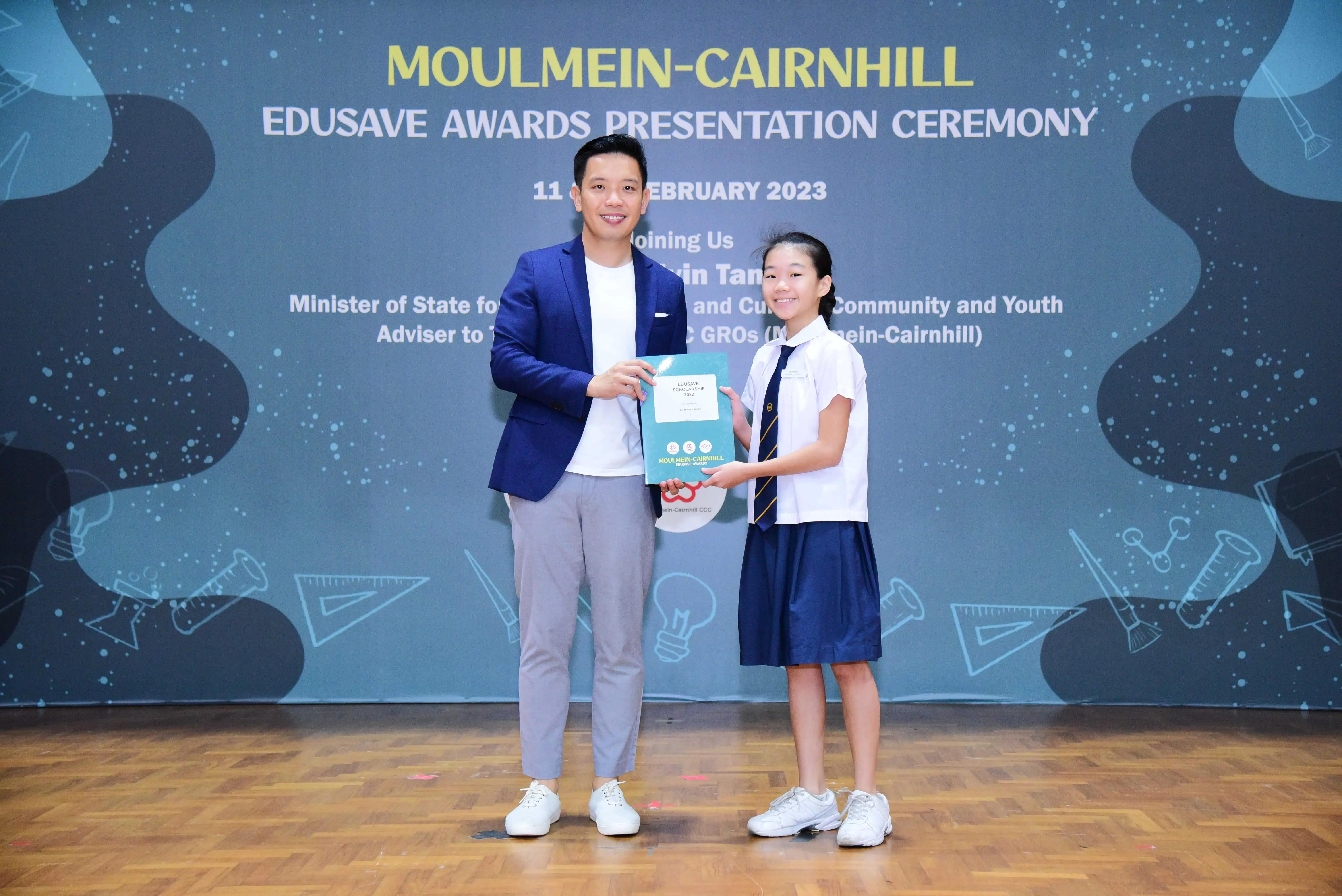 Man in blue blazer and young girl in school uniform hold a certificate at Moulmein-Cairnhill Edusave Awards 2023.