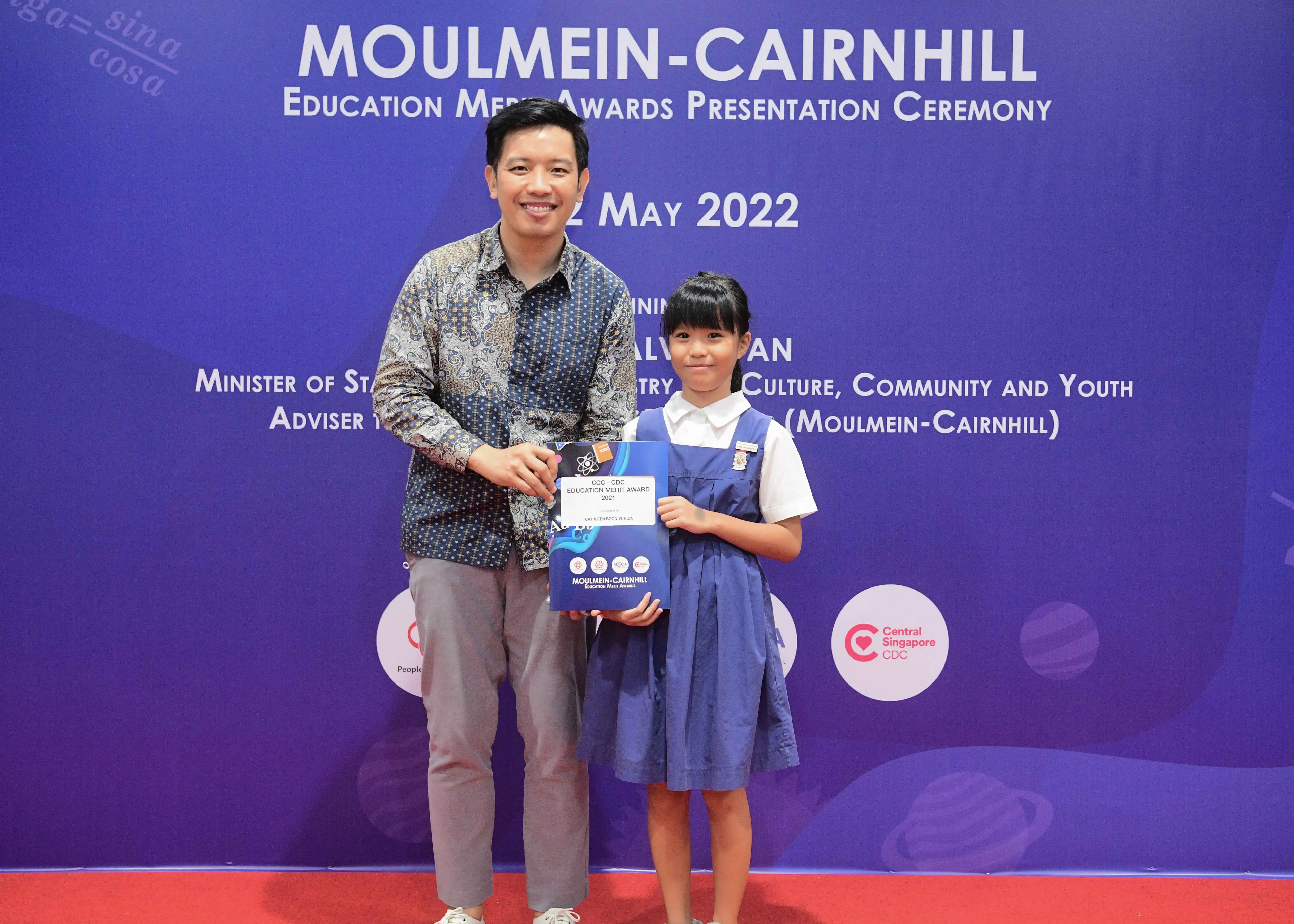 Man and young girl pose holding an award certificate at the Moulmein-Cairnhill Education Merit Awards, May 2022.