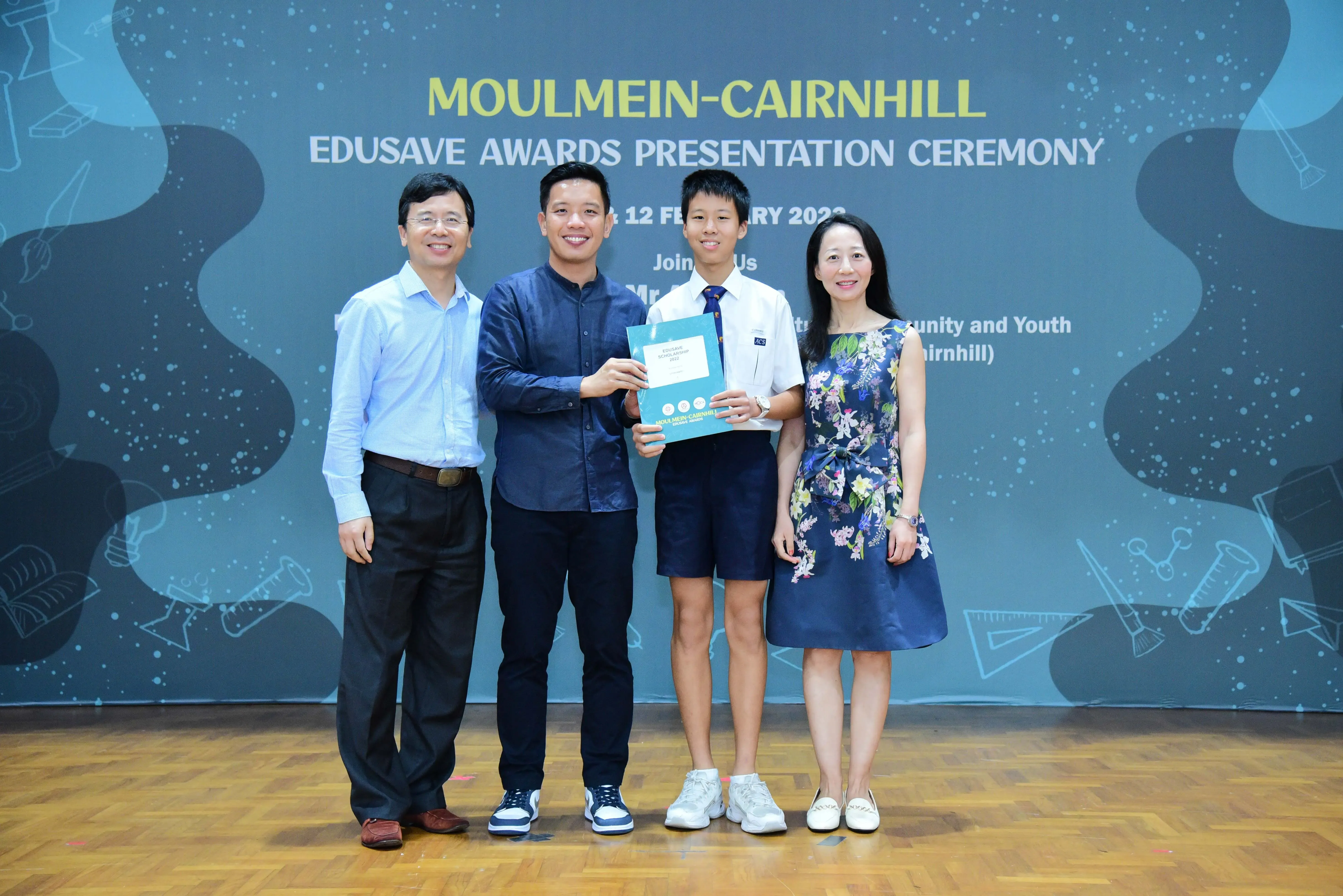 Four people pose at the Moulmein-Cairnhill Edusave Awards Presentation Ceremony, with a student holding a certificate.