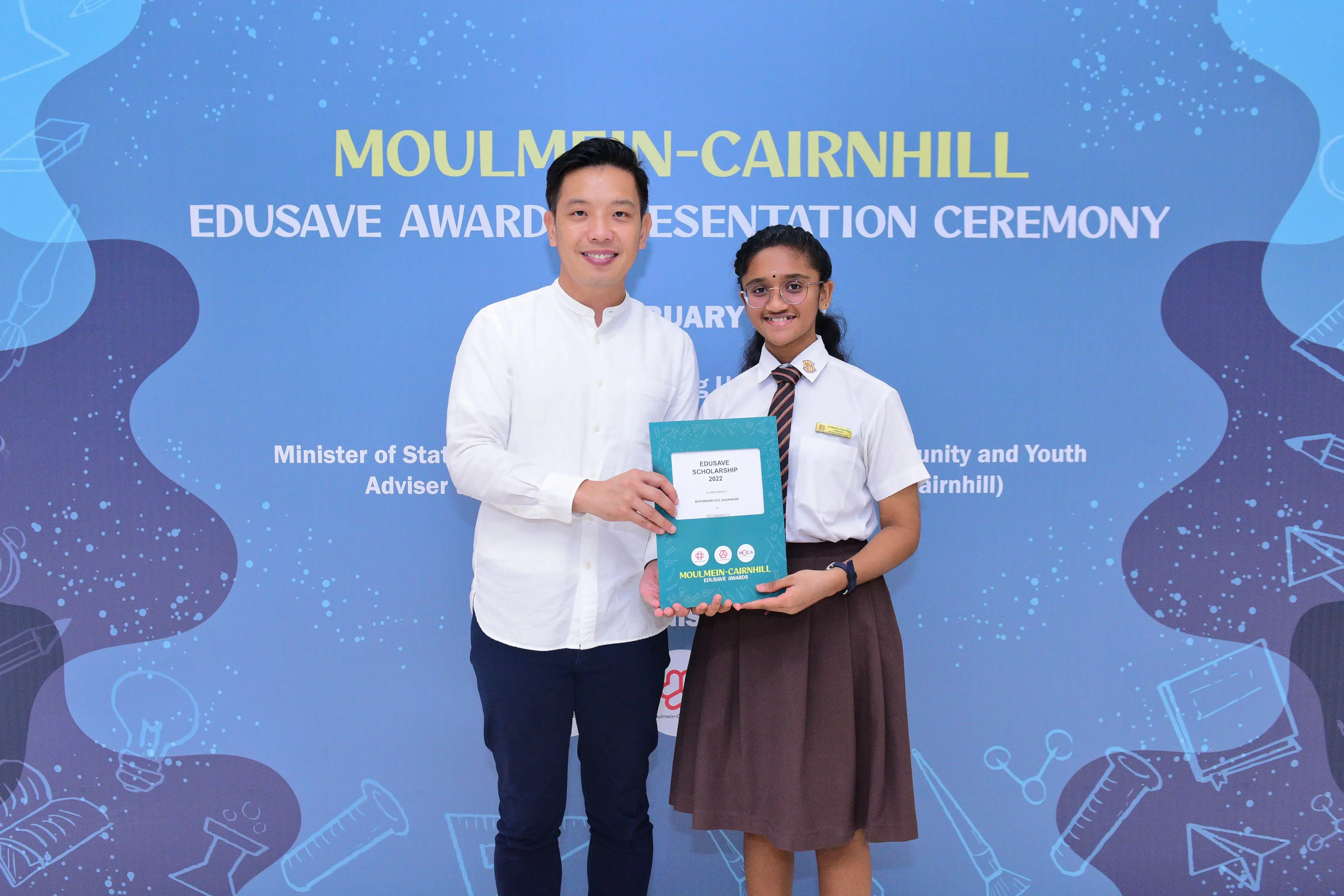 Two people hold a teal Edusave Scholarship booklet at the Moulmein-Cairnhill Edusave Awards Presentation Ceremony.