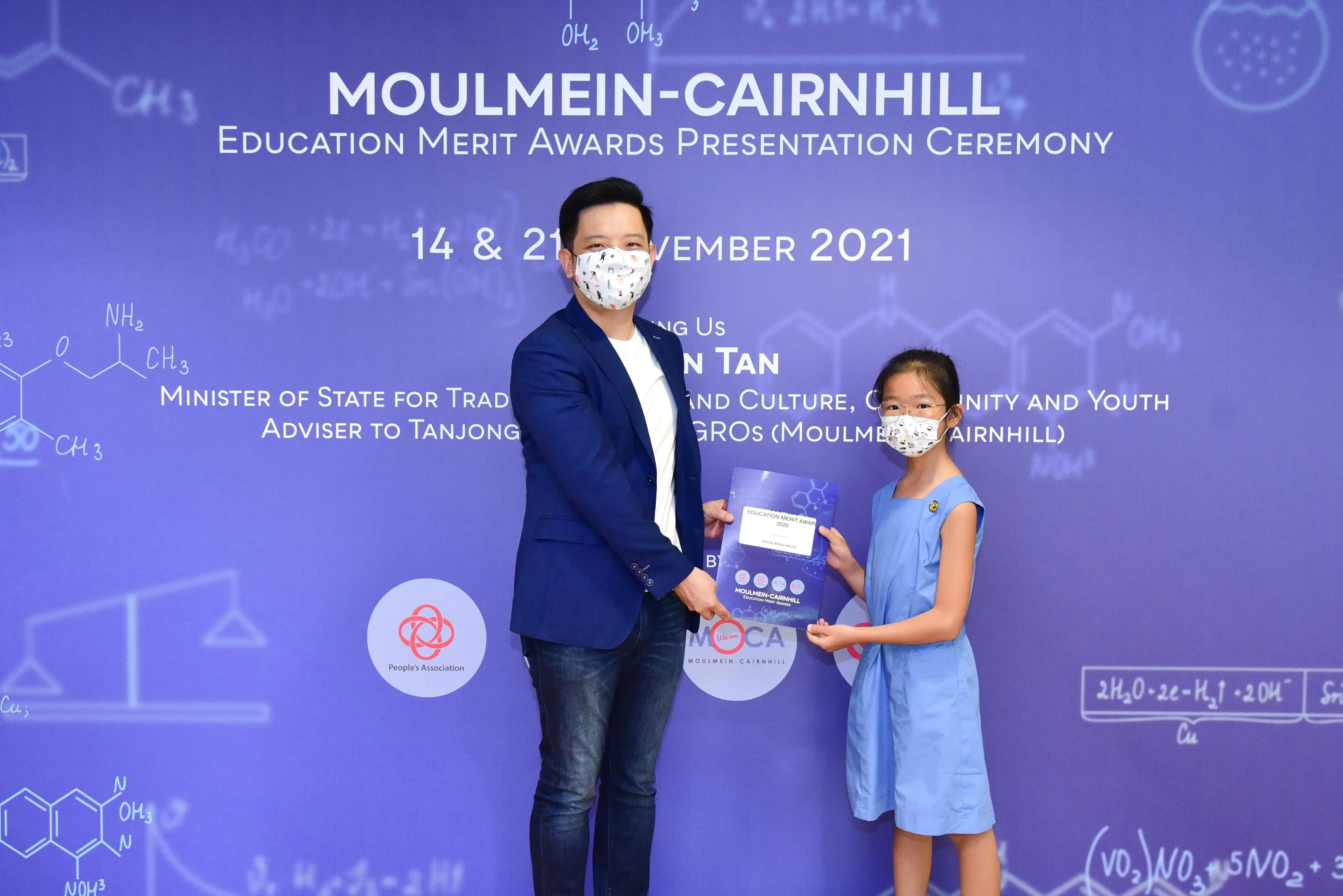 A masked man and young girl hold a certificate at the Moulmein-Cairnhill Education Merit Awards Ceremony 2021.
