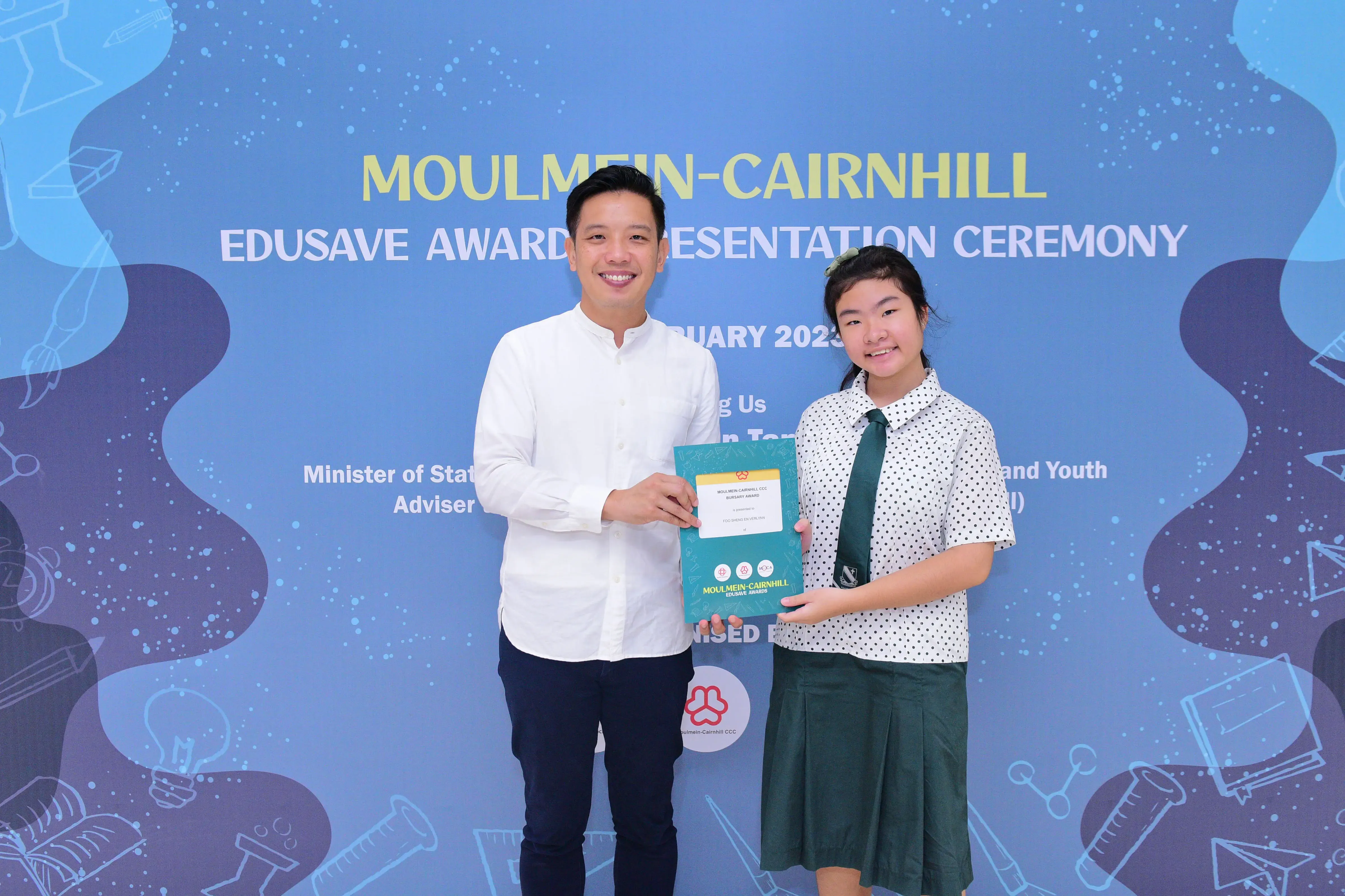 A man and a young girl hold a certificate together at the Moulmein-Cairnhill Edusave Awards Presentation Ceremony 2023.