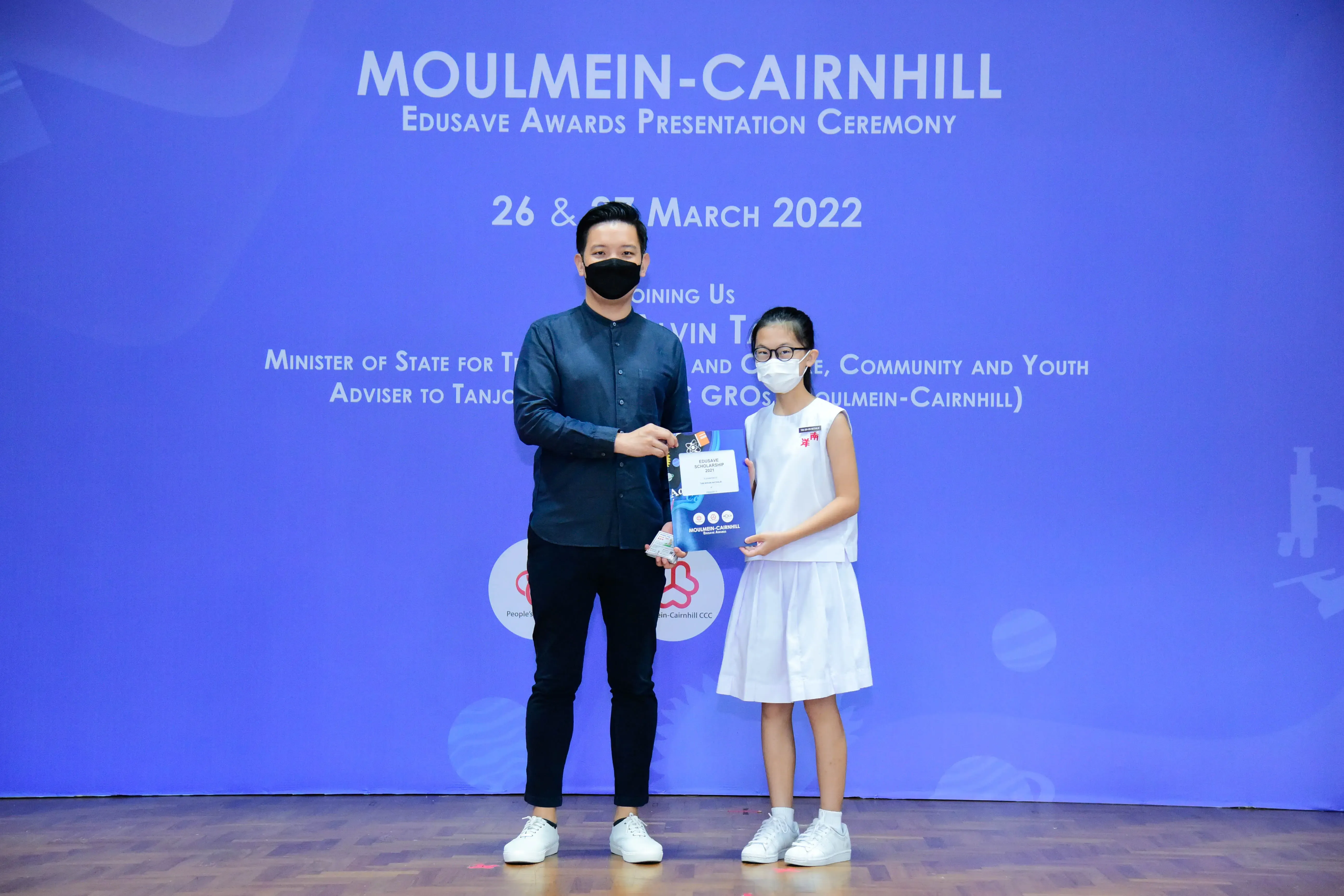 Man and young girl in masks holding an award at the Moulmein-Cairnhill Edusave Awards Ceremony, March 2022.
