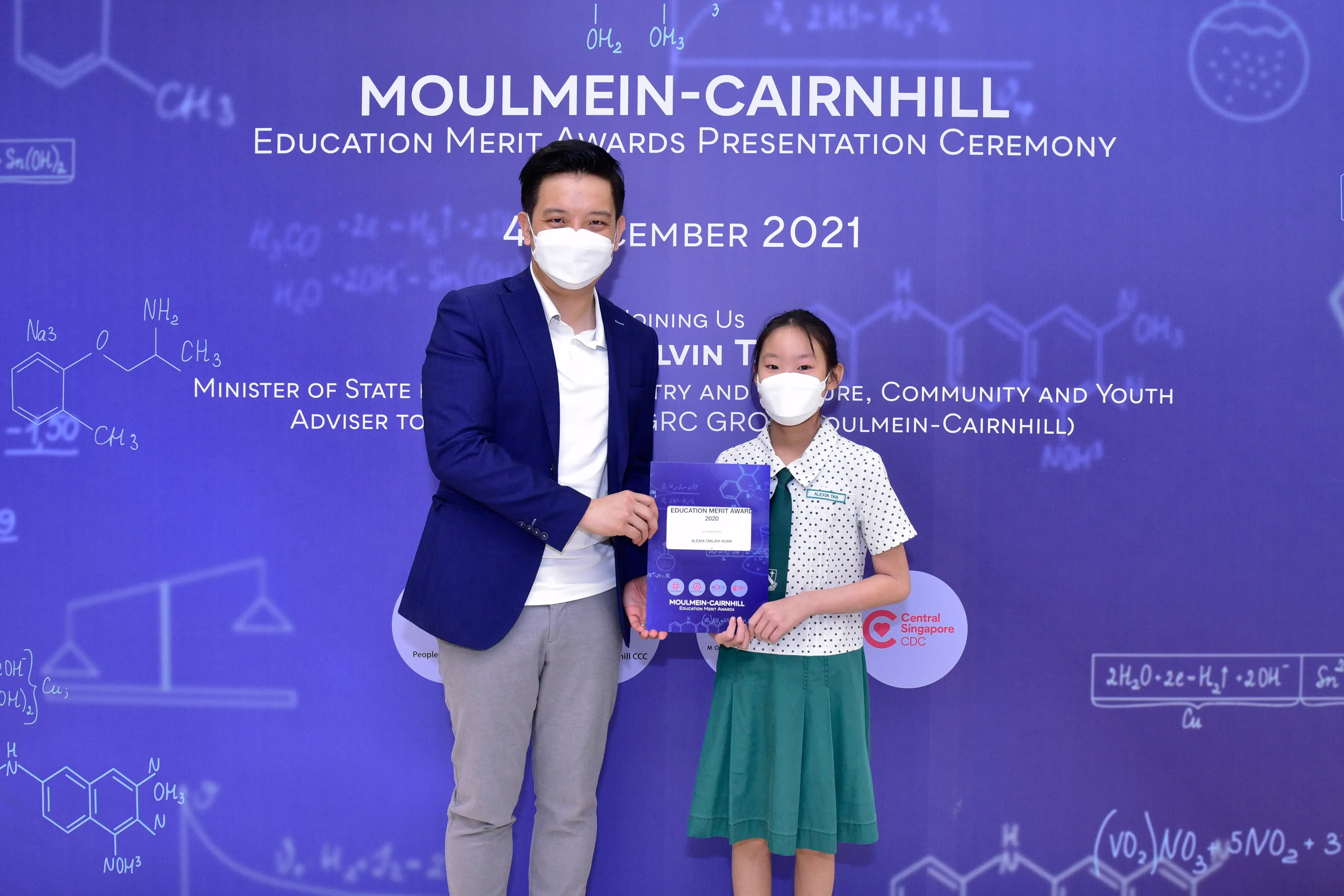A masked man and a young girl hold an award certificate at the Moulmein-Cairnhill Education Merit Awards 2021.