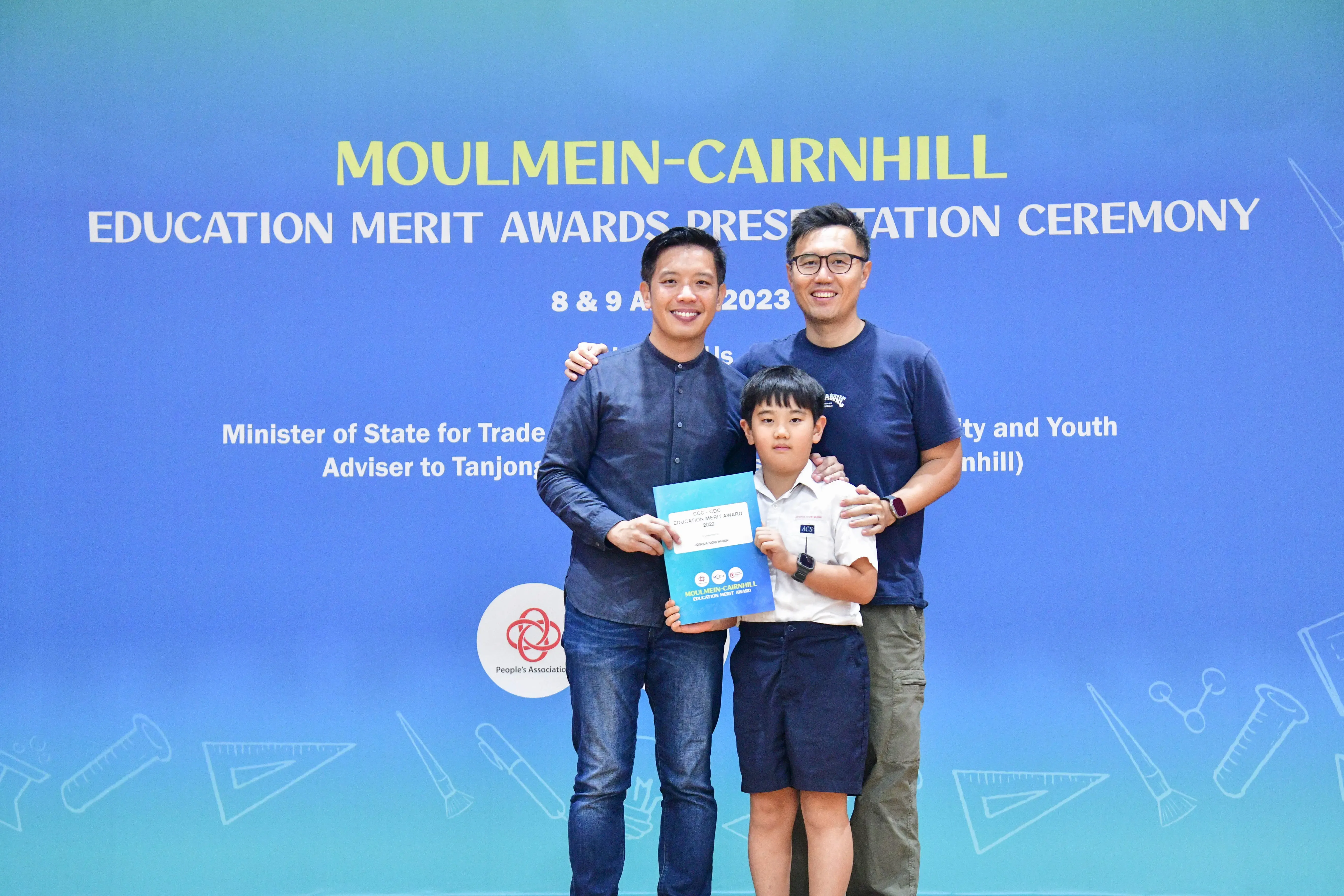 Two men and a boy holding an award certificate pose at the Moulmein-Cairnhill Education Merit Awards Ceremony 2023.