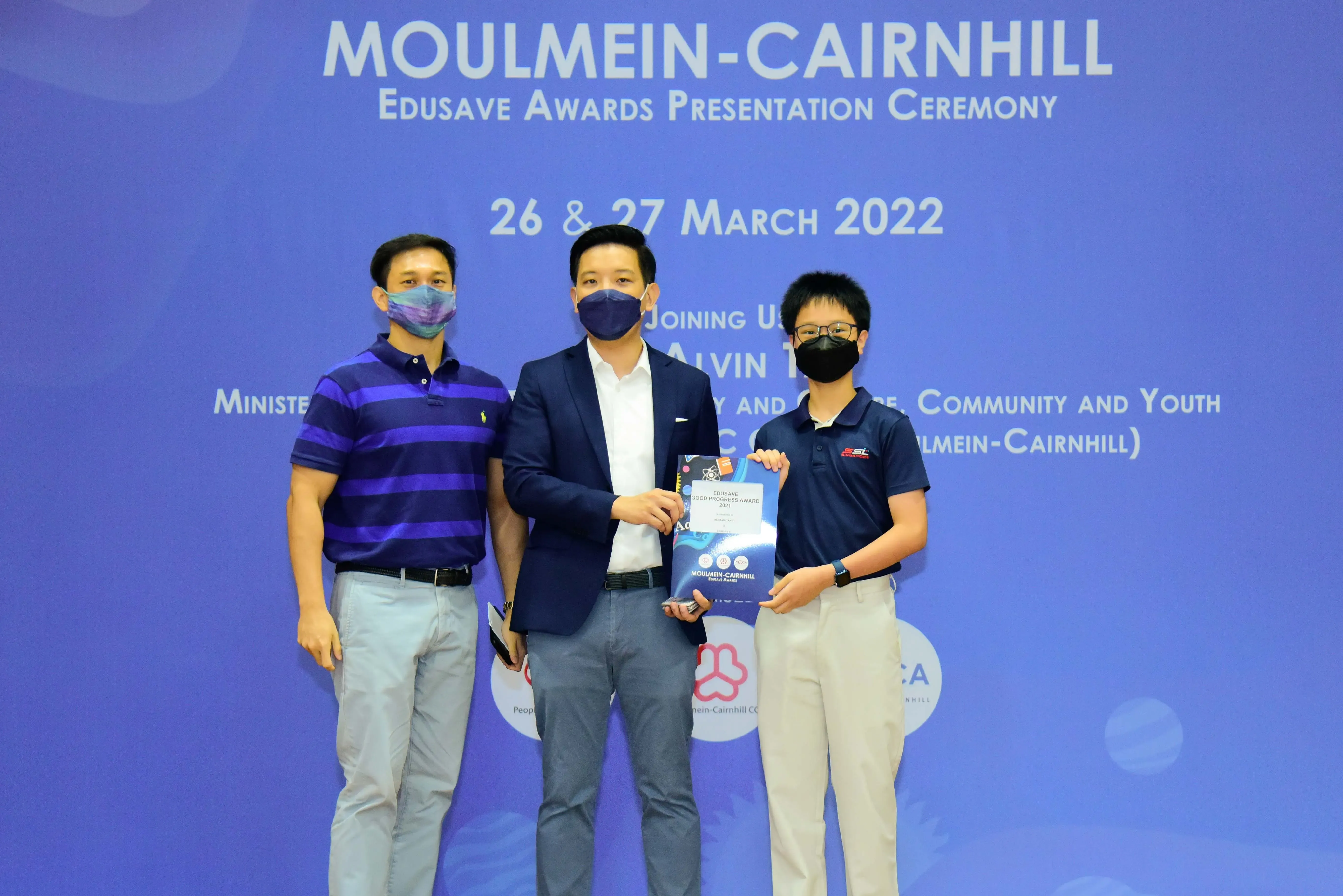 Three masked people pose holding an award at the Moulmein-Cairnhill Edusave Awards Presentation Ceremony, March 2022.