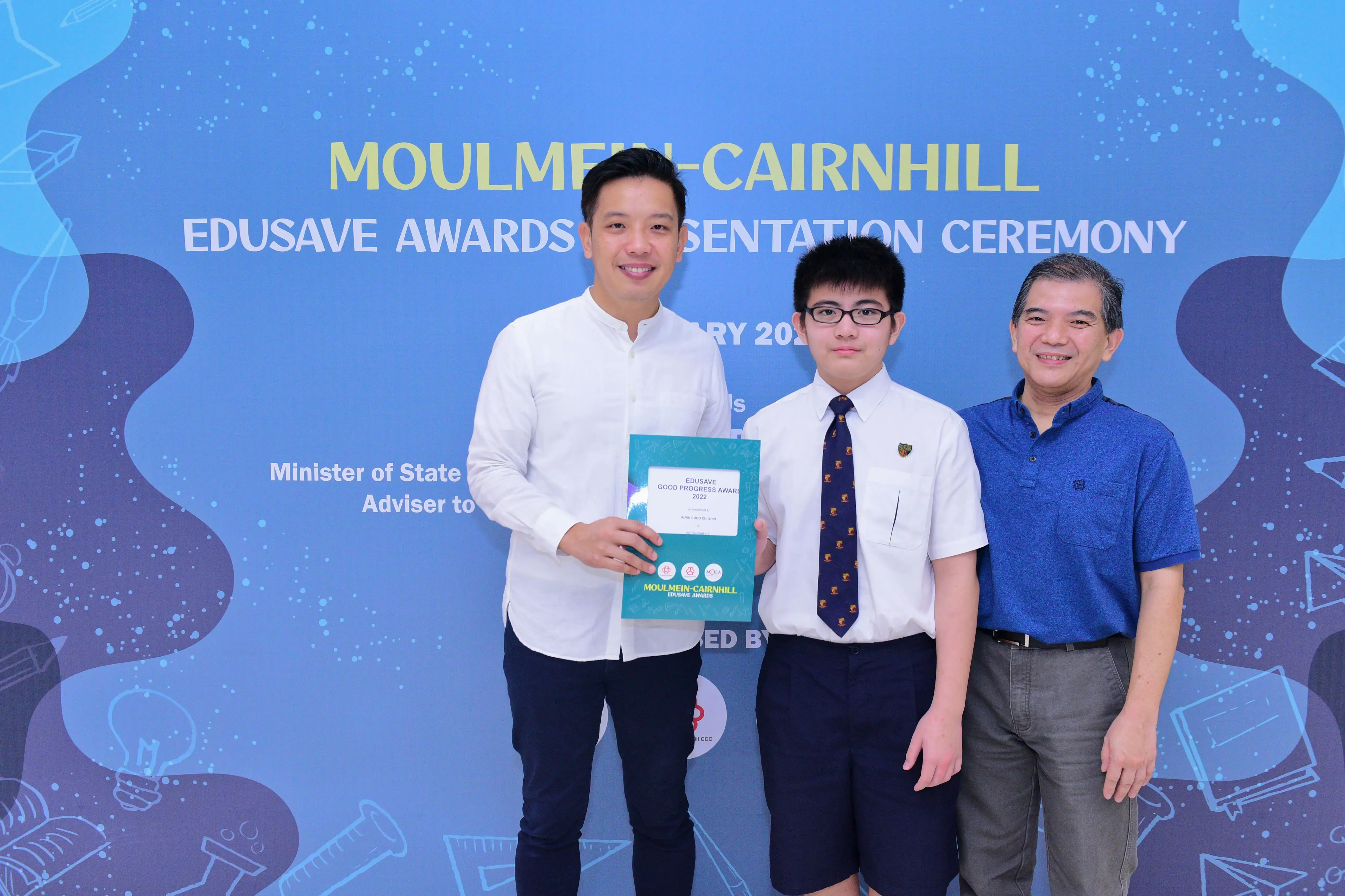 Three men pose at the Moulmein-Cairnhill Edusave Awards Presentation Ceremony, holding a certificate.