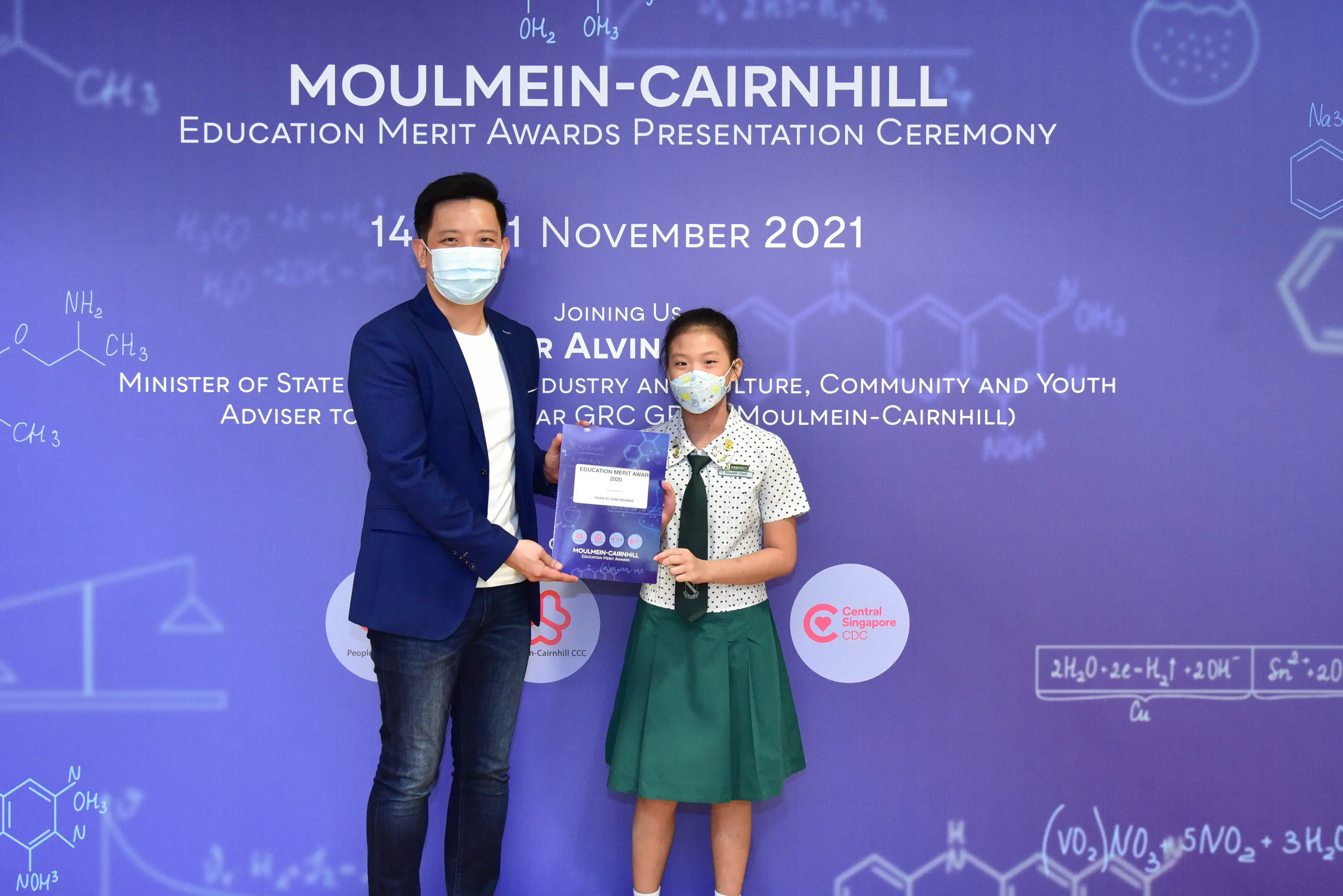 A man and a young girl in school uniform hold an award certificate at the Moulmein-Cairnhill Education Merit Awards 2021.