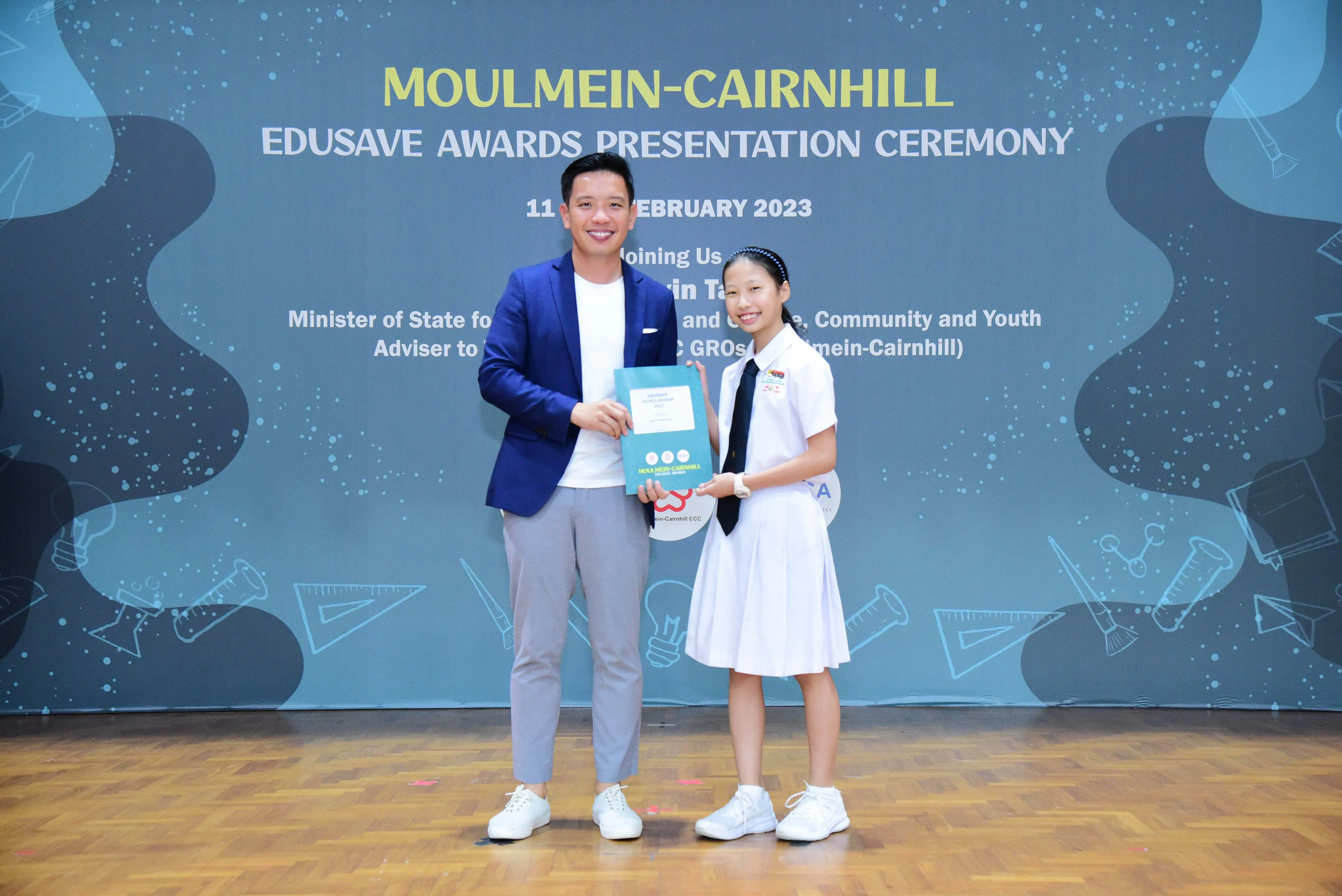 A man in a blue blazer and a girl in school uniform hold an award at the Moulmein-Cairnhill Edusave Awards Ceremony 2023.