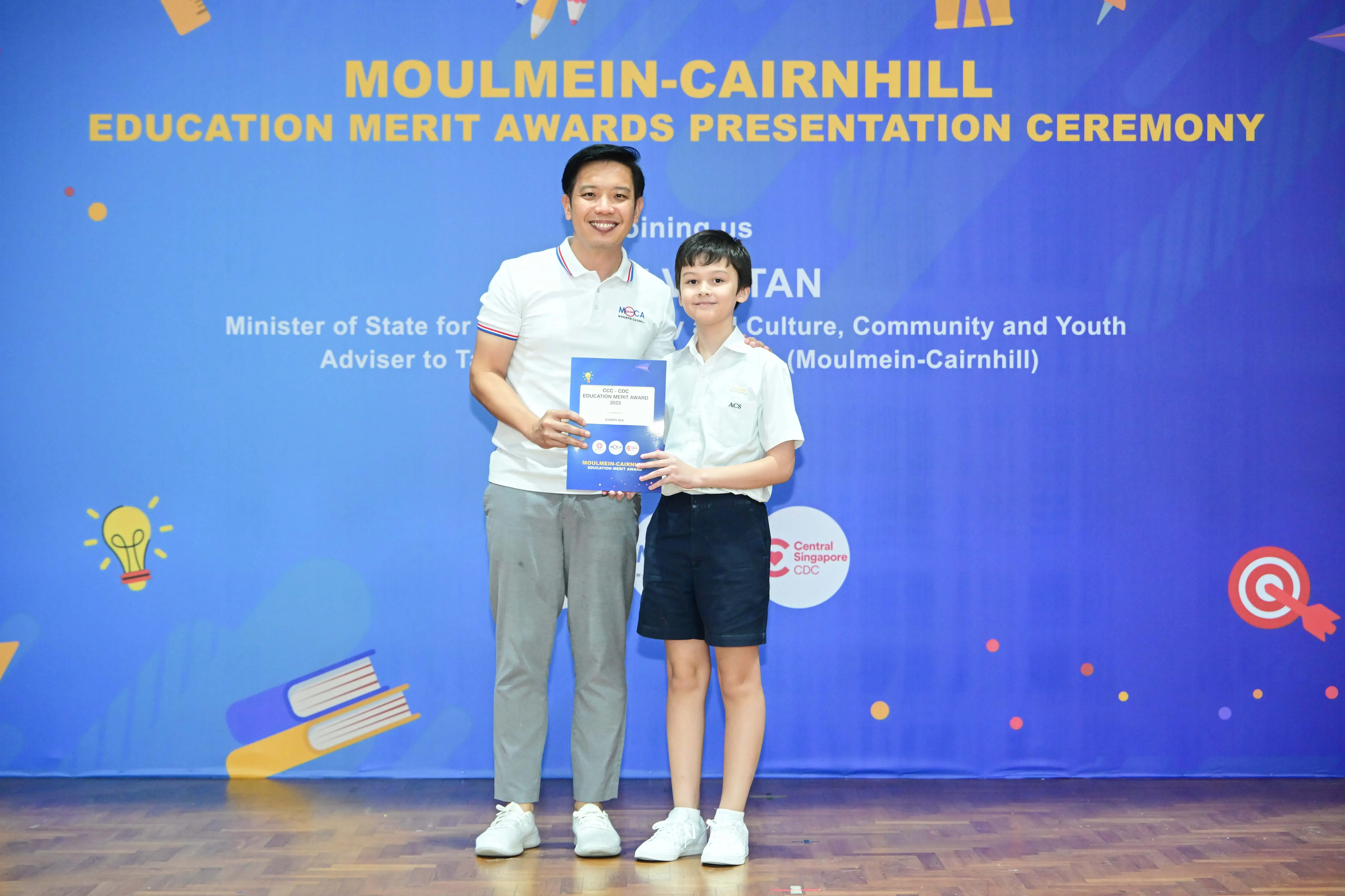 Man and young boy hold a certificate at the Moulmein-Cairnhill Education Merit Awards Presentation Ceremony.