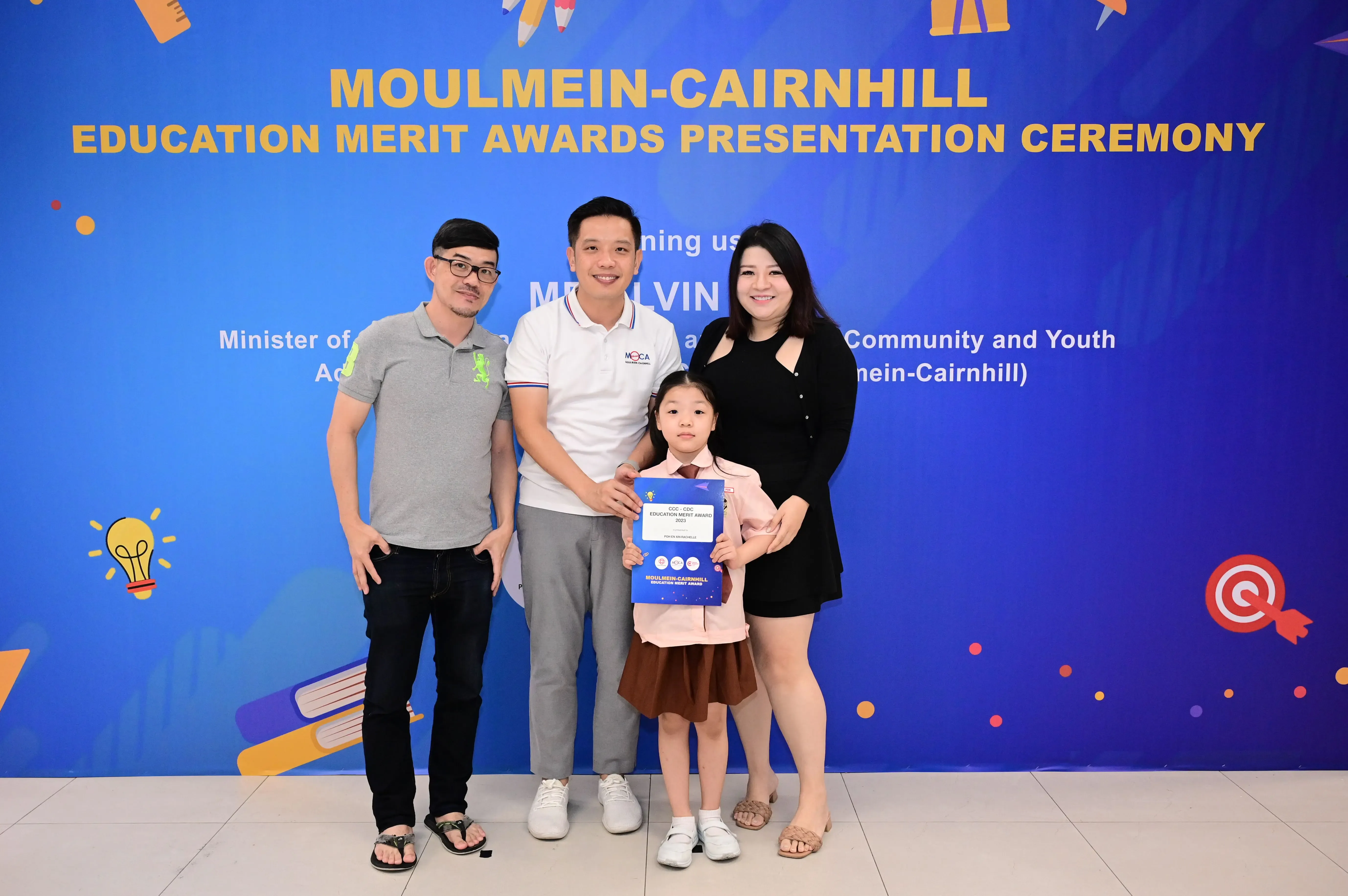 Three adults and a young girl holding a certificate pose at Moulmein-Cairnhill Education Merit Awards ceremony.