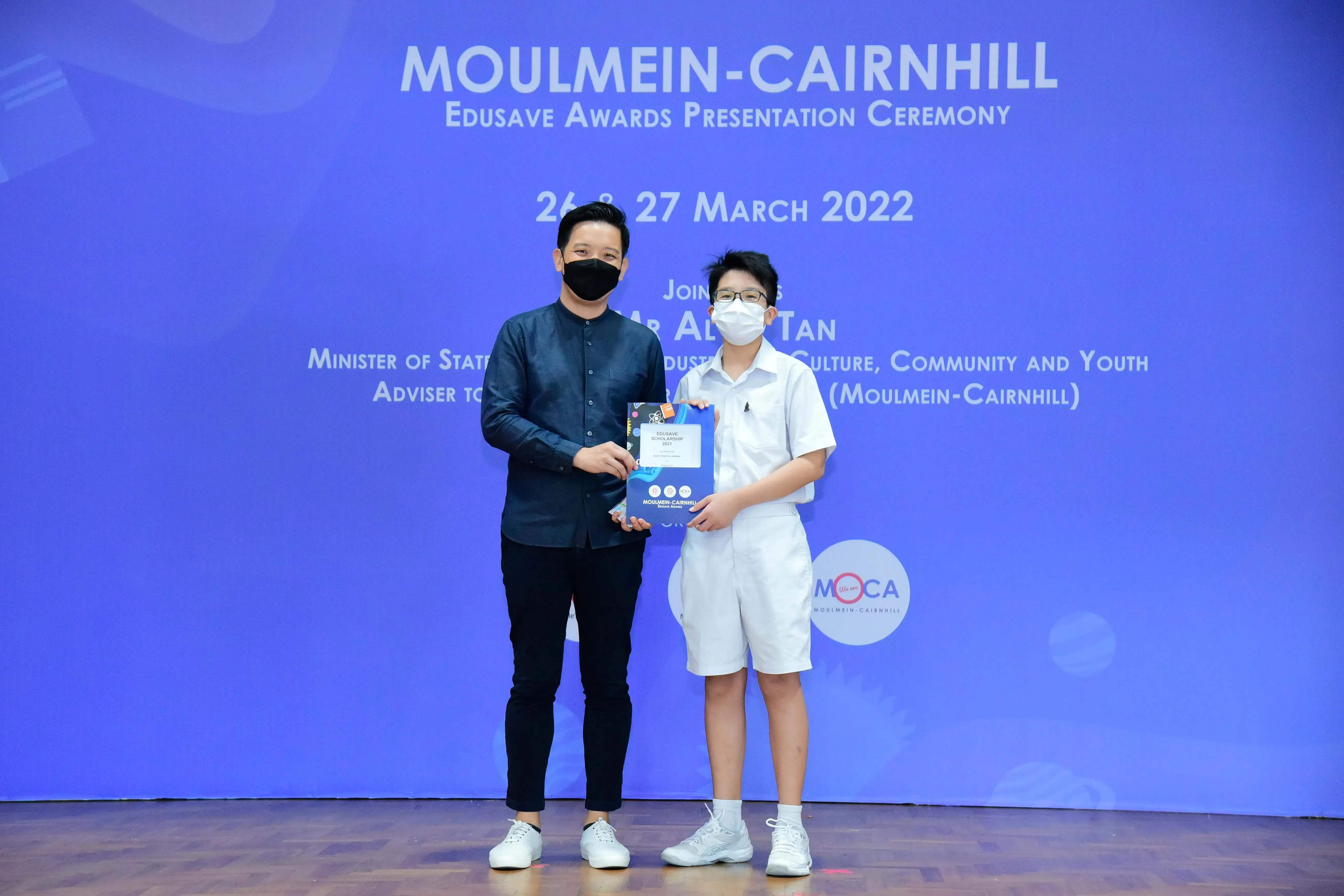Two masked individuals hold an award at the Moulmein-Cairnhill Edusave Awards Presentation Ceremony, March 2022.