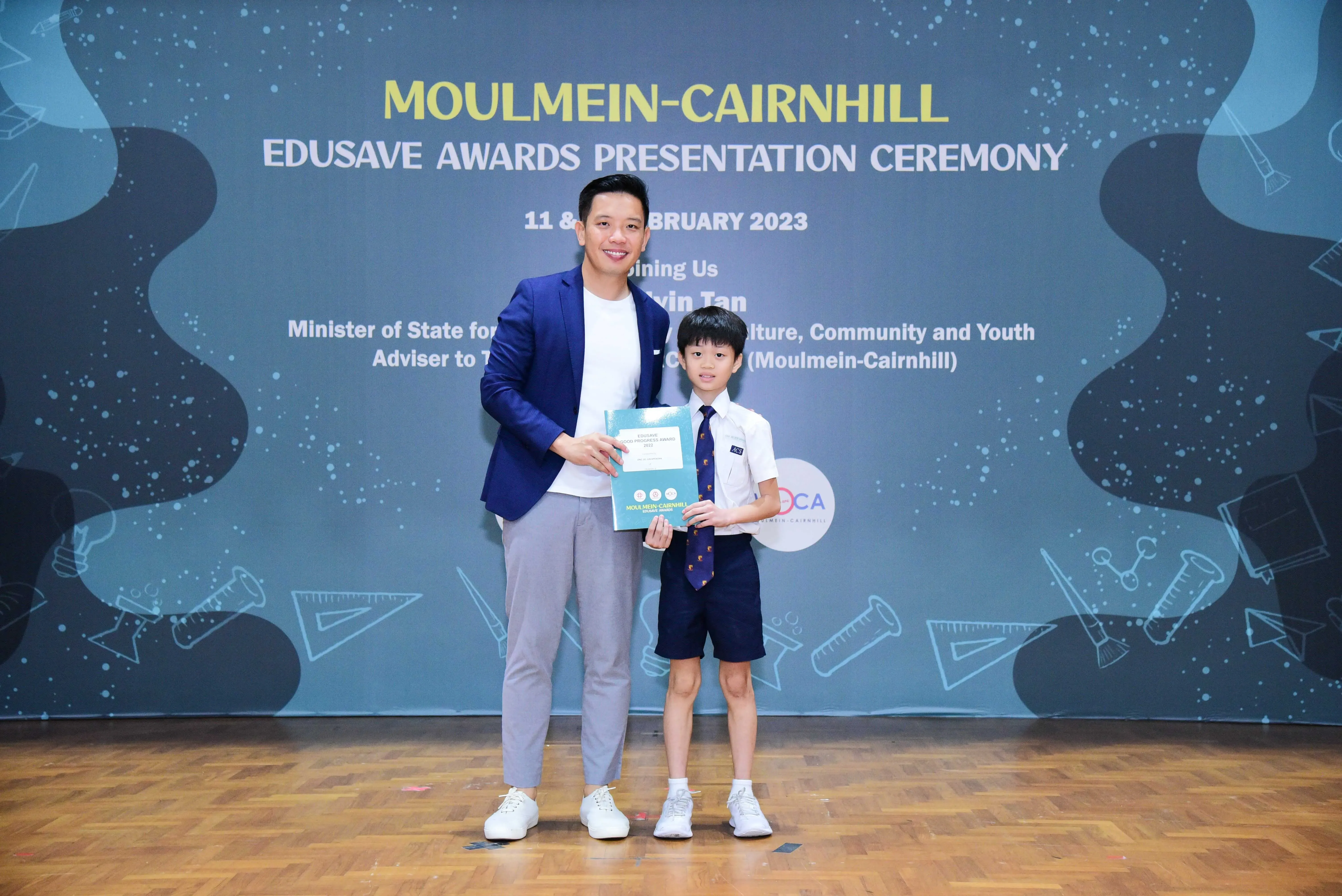 Man in blue blazer and young boy in school uniform hold a certificate at Moulmein-Cairnhill Edusave Awards 2023.