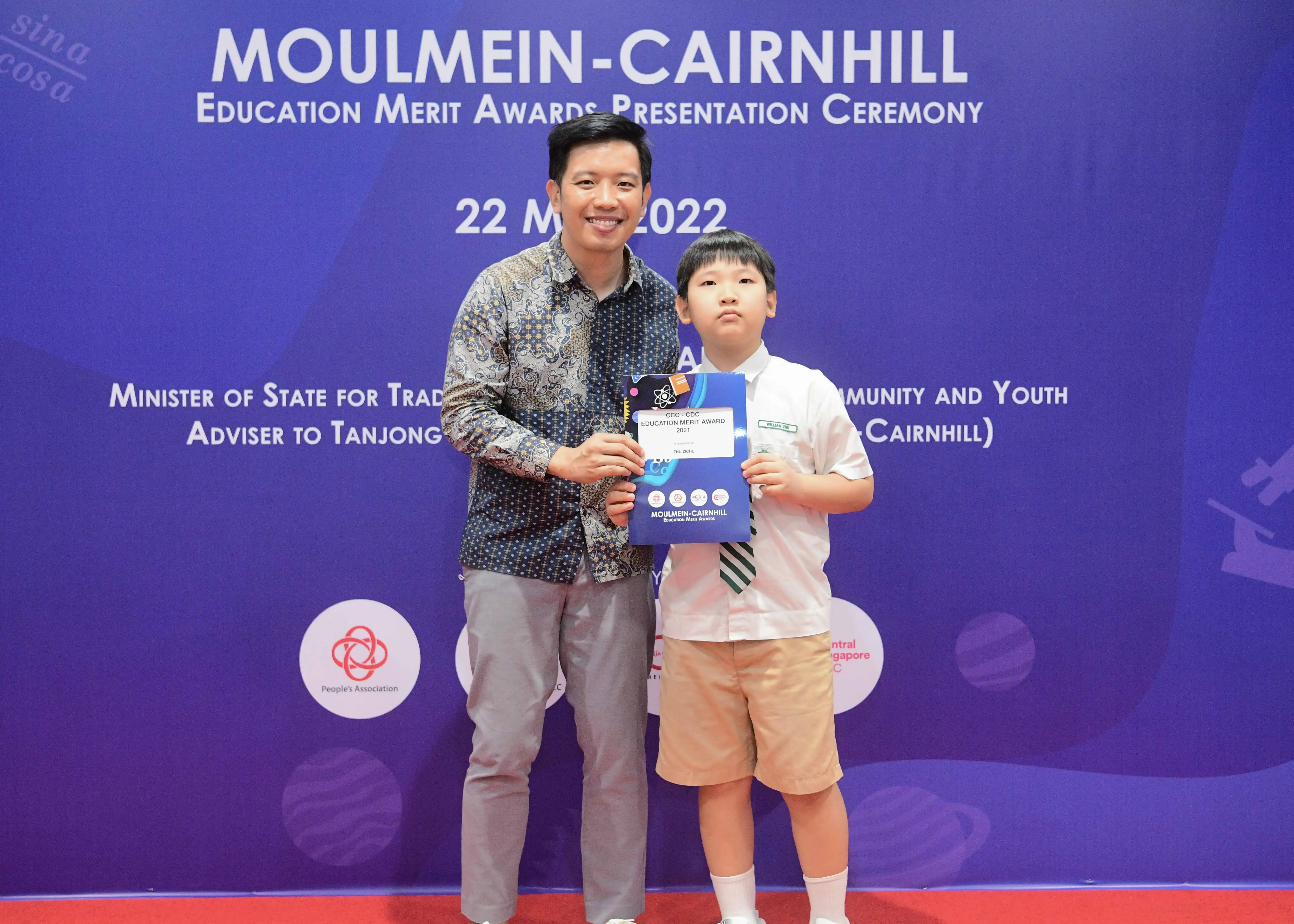 A man and a young boy pose holding an award certificate at the Moulmein-Cairnhill Education Merit Awards Ceremony 2022.