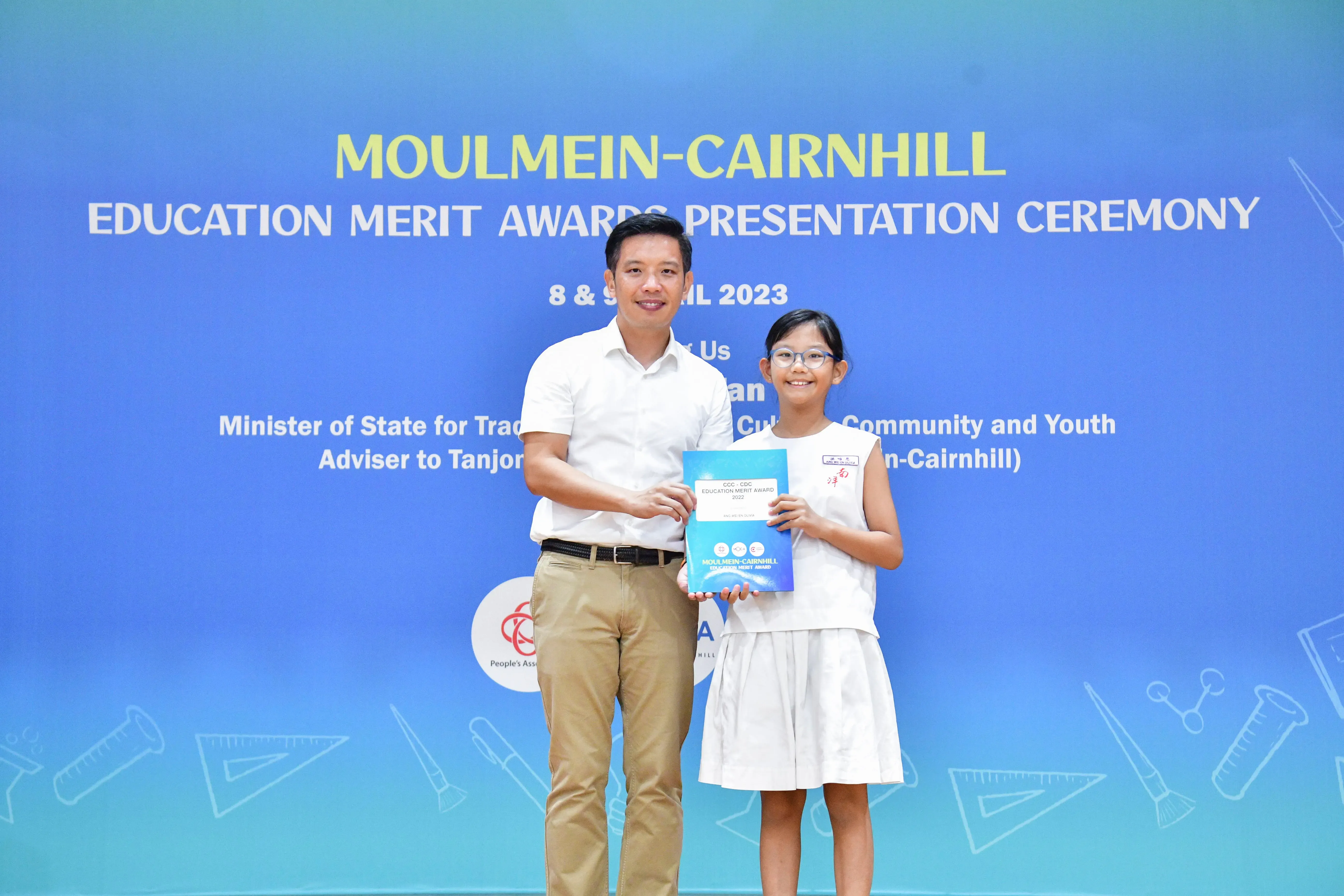 A man and a young girl hold a blue award booklet at the Moulmein-Cairnhill Education Merit Awards 2023.