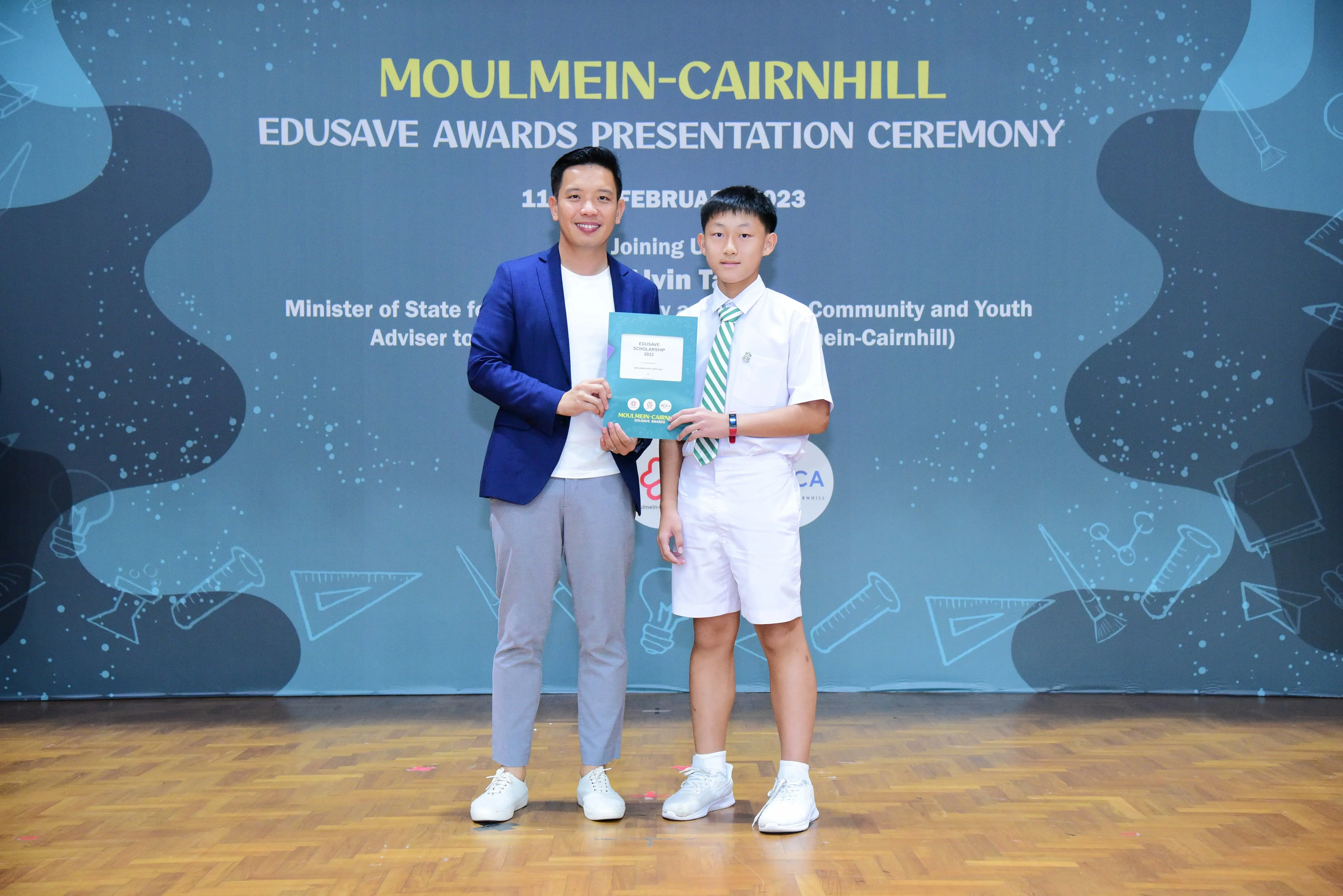 Man in blue blazer and young boy in school uniform hold an award at Moulmein-Cairnhill Edusave Awards Ceremony 2023.