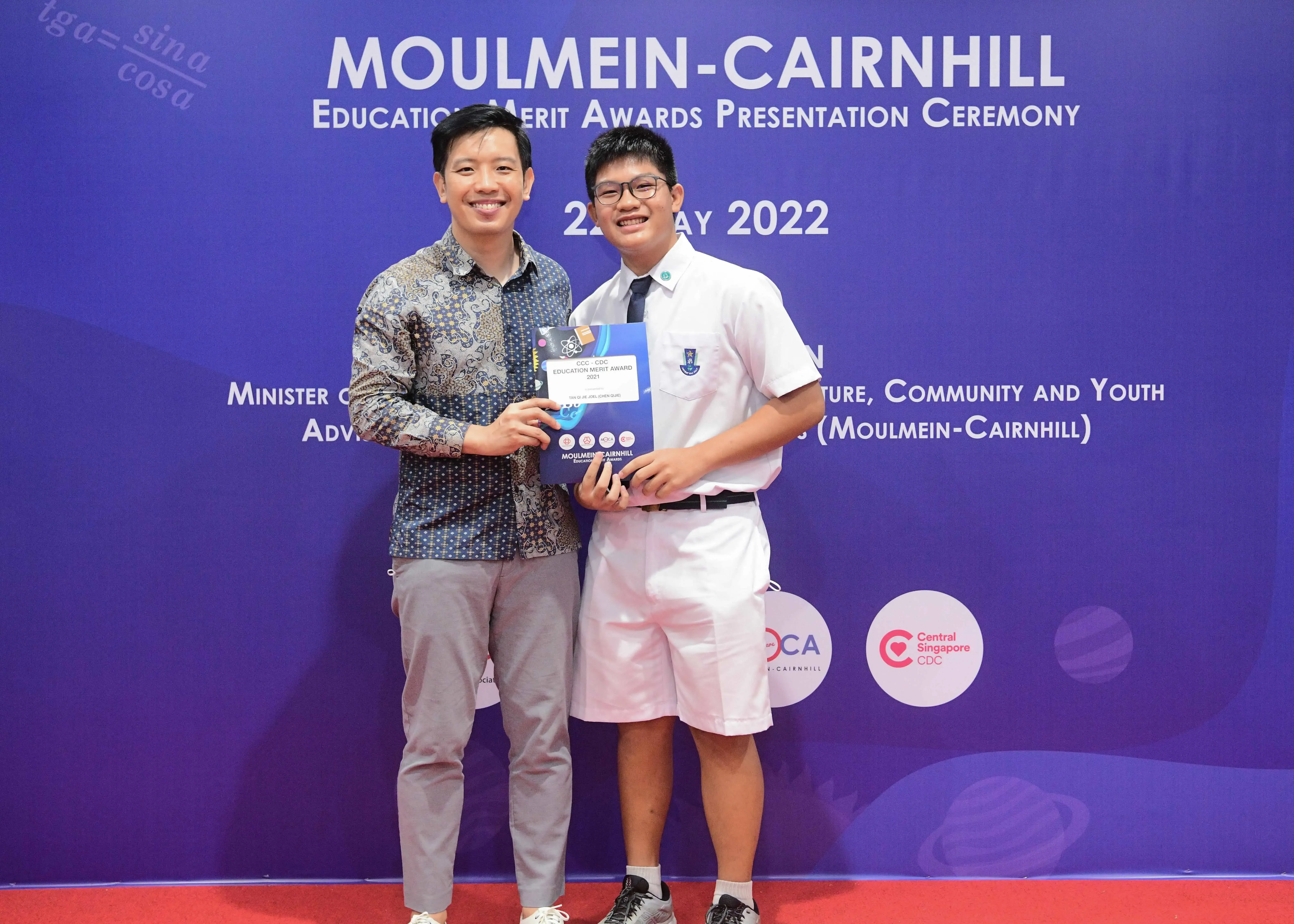 Two smiling men hold an award at the Moulmein-Cairnhill Education Merit Awards Presentation Ceremony 2022.