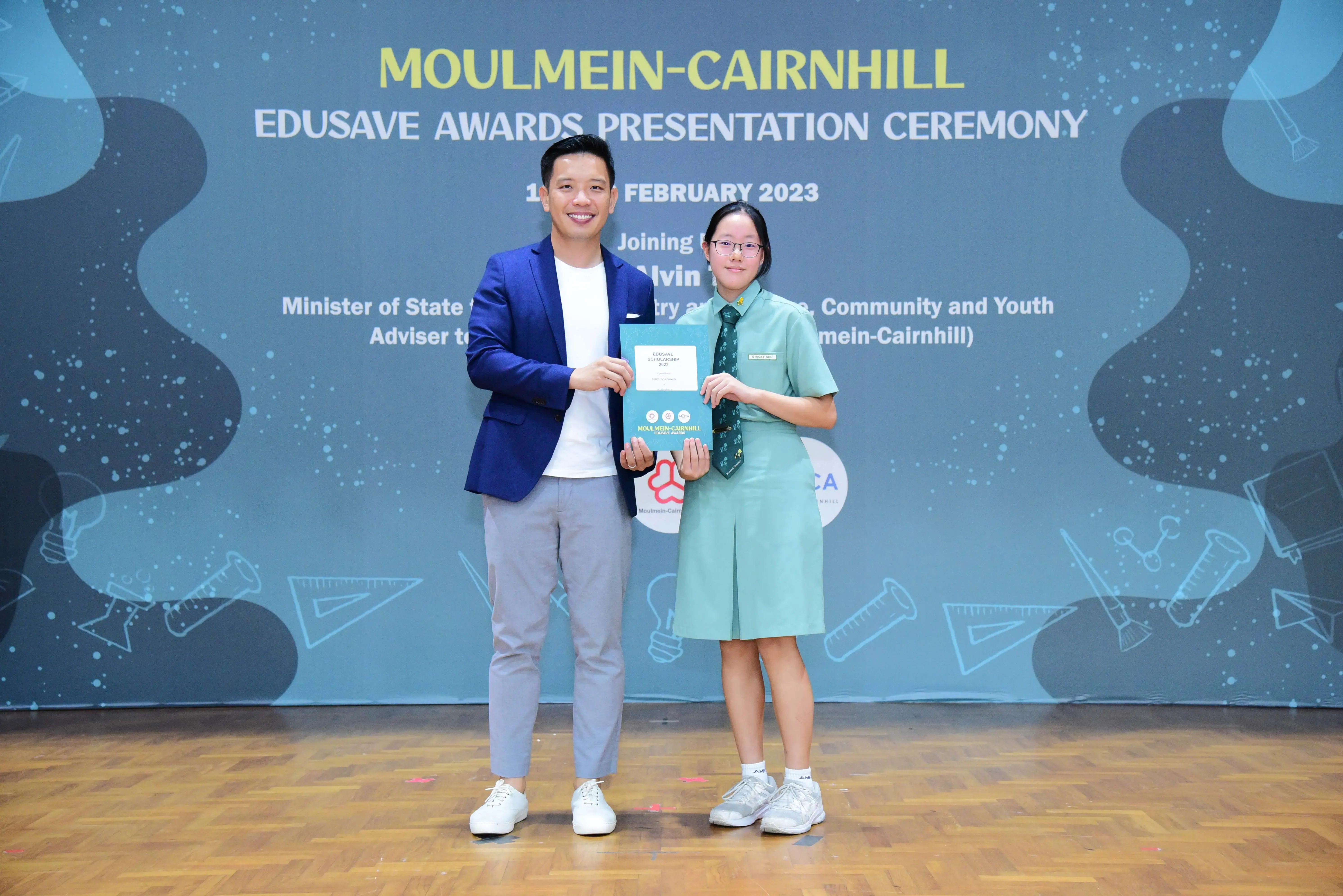 A man in a blue blazer and a girl in school uniform hold an award at the Moulmein-Cairnhill Edusave Awards Ceremony 2023.