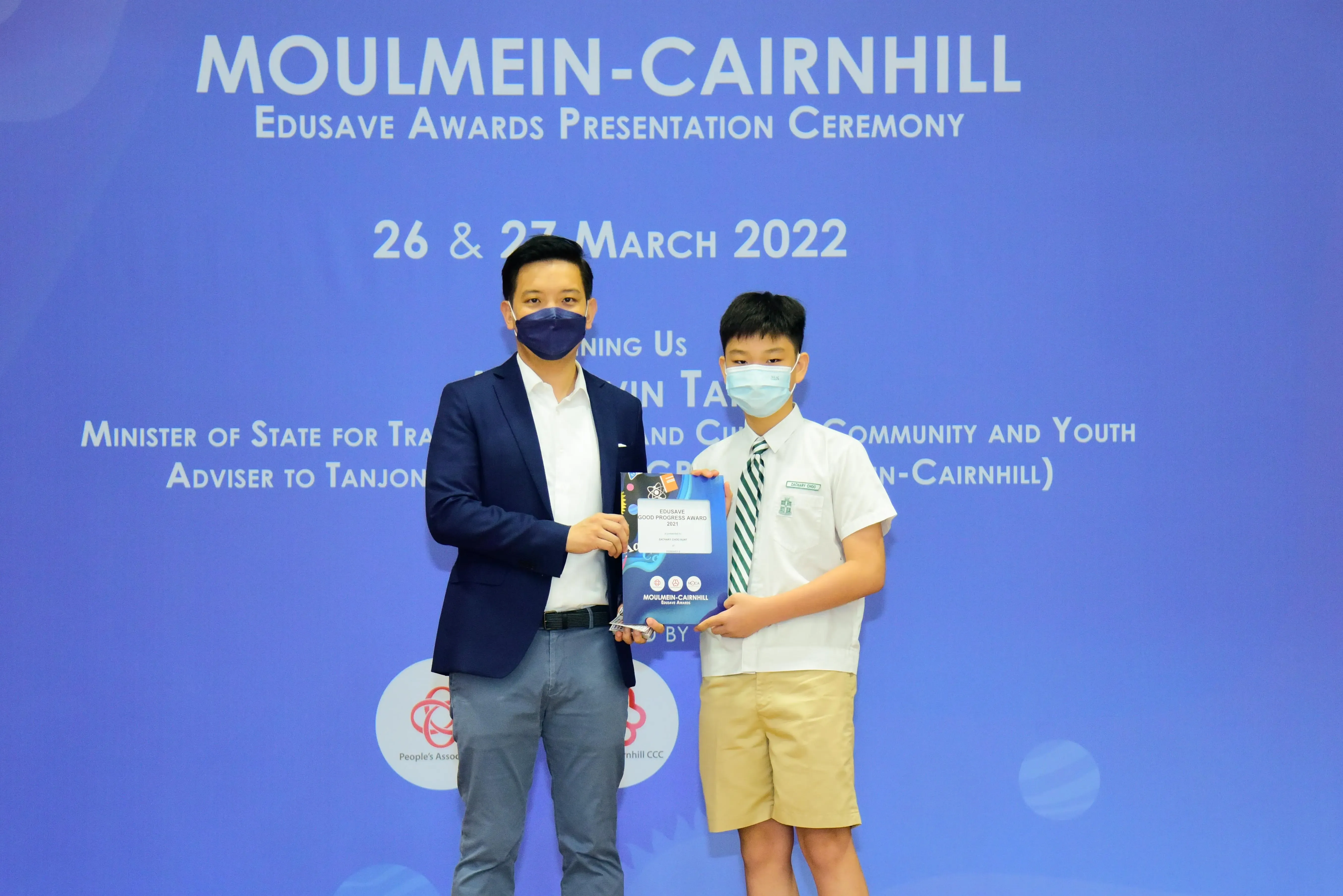 Two masked individuals hold an award certificate at the Moulmein-Cairnhill Edusave Awards Presentation Ceremony, March 2022.