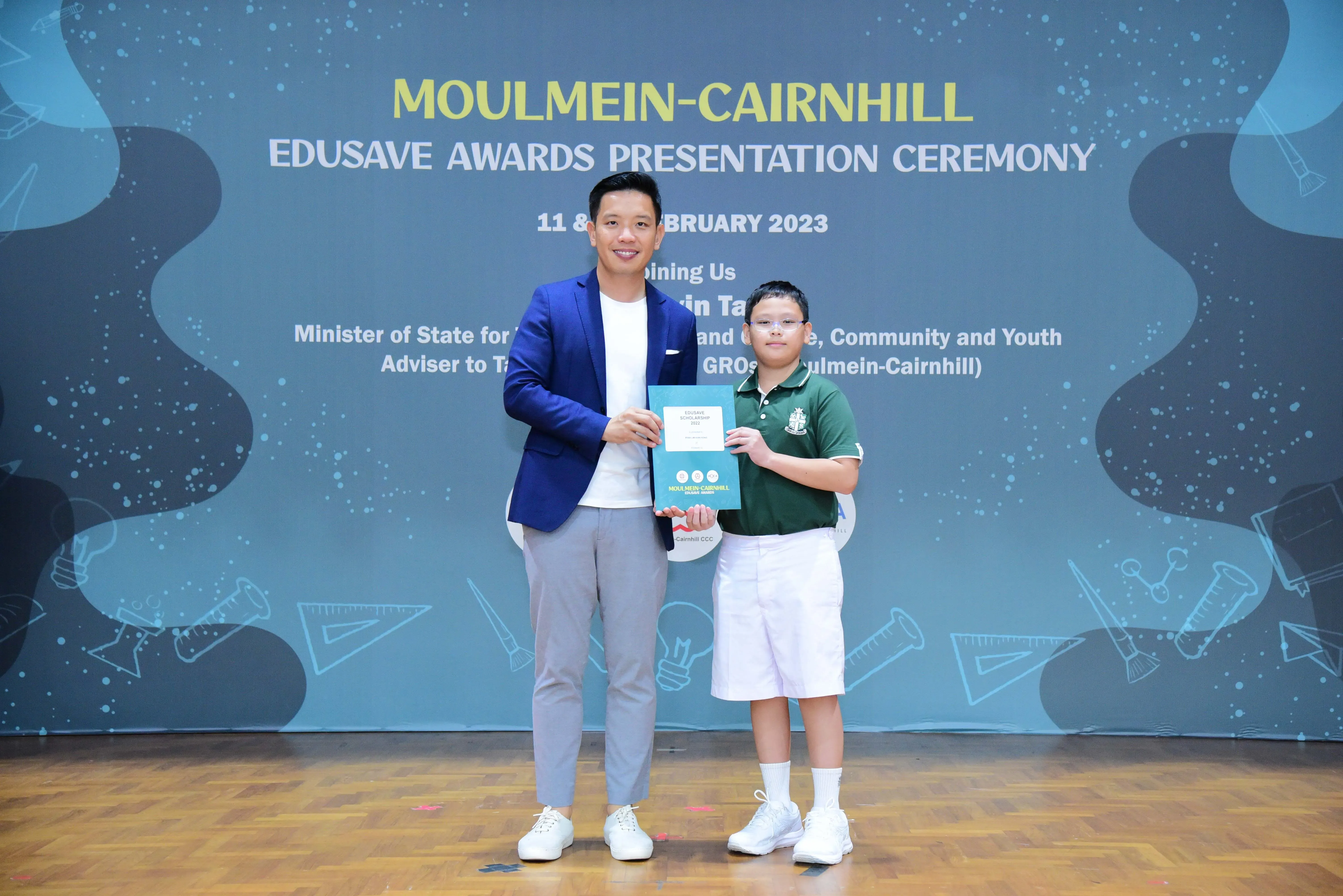 Man in blue blazer and young boy holding a certificate at Moulmein-Cairnhill Edusave Awards Ceremony 2023.