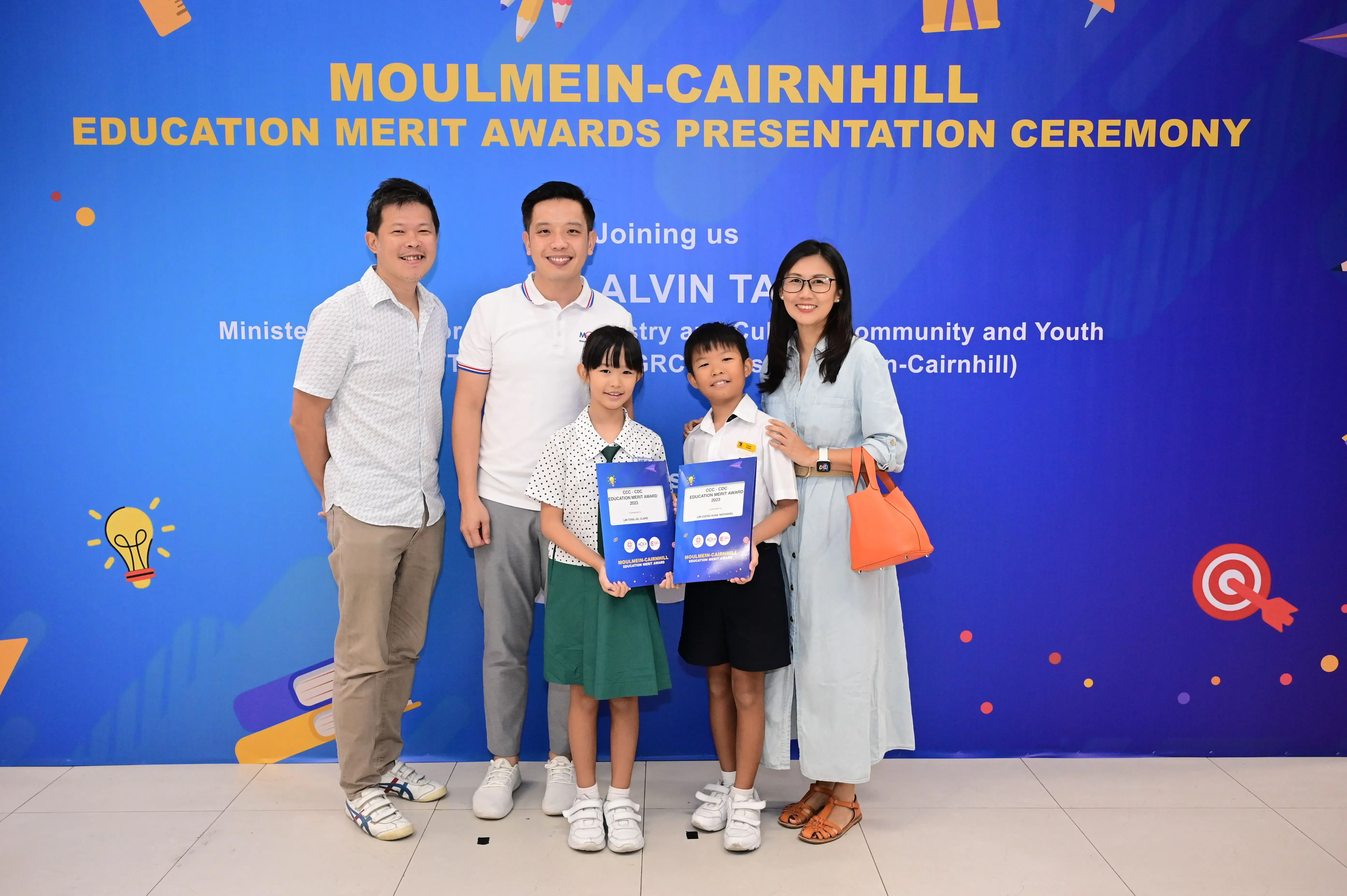 Two adults and two children pose holding award certificates at the Moulmein-Cairnhill Education Merit Awards ceremony.
