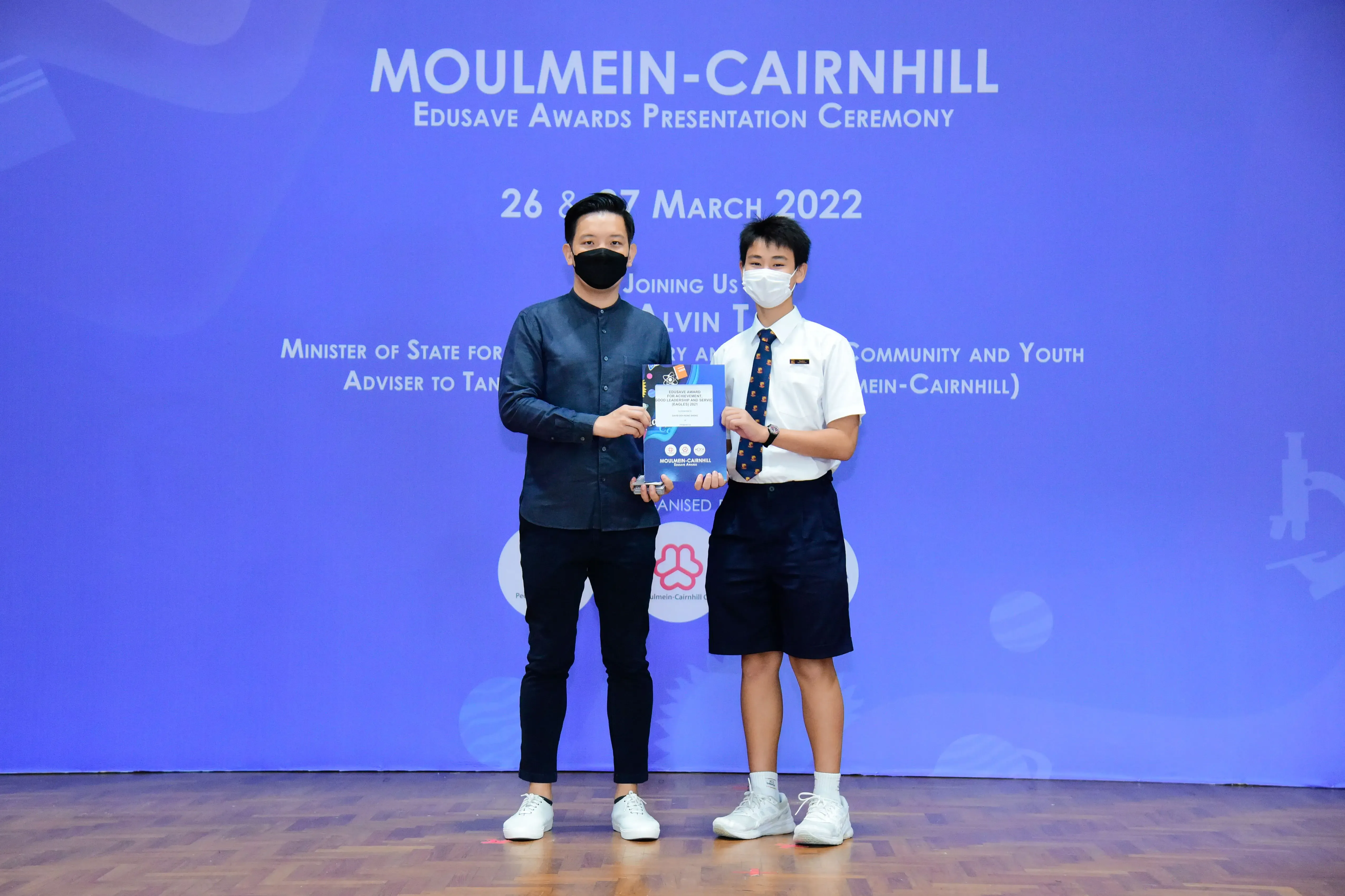 Two masked individuals hold an award booklet at the Moulmein-Cairnhill Edusave Awards Ceremony, March 2022.
