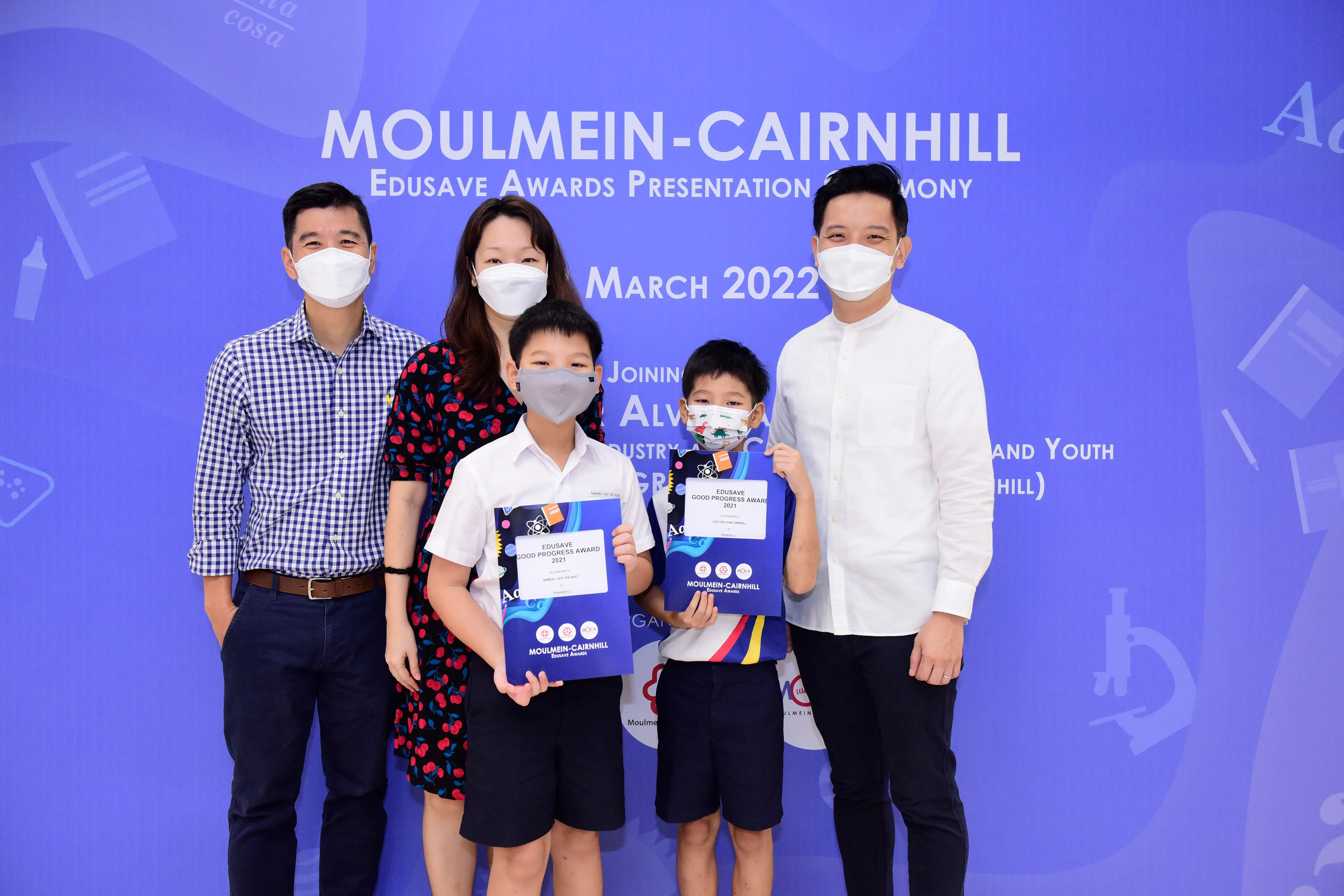Five masked people pose at the Moulmein-Cairnhill Edusave Awards ceremony in March 2022, two boys holding award certificates.