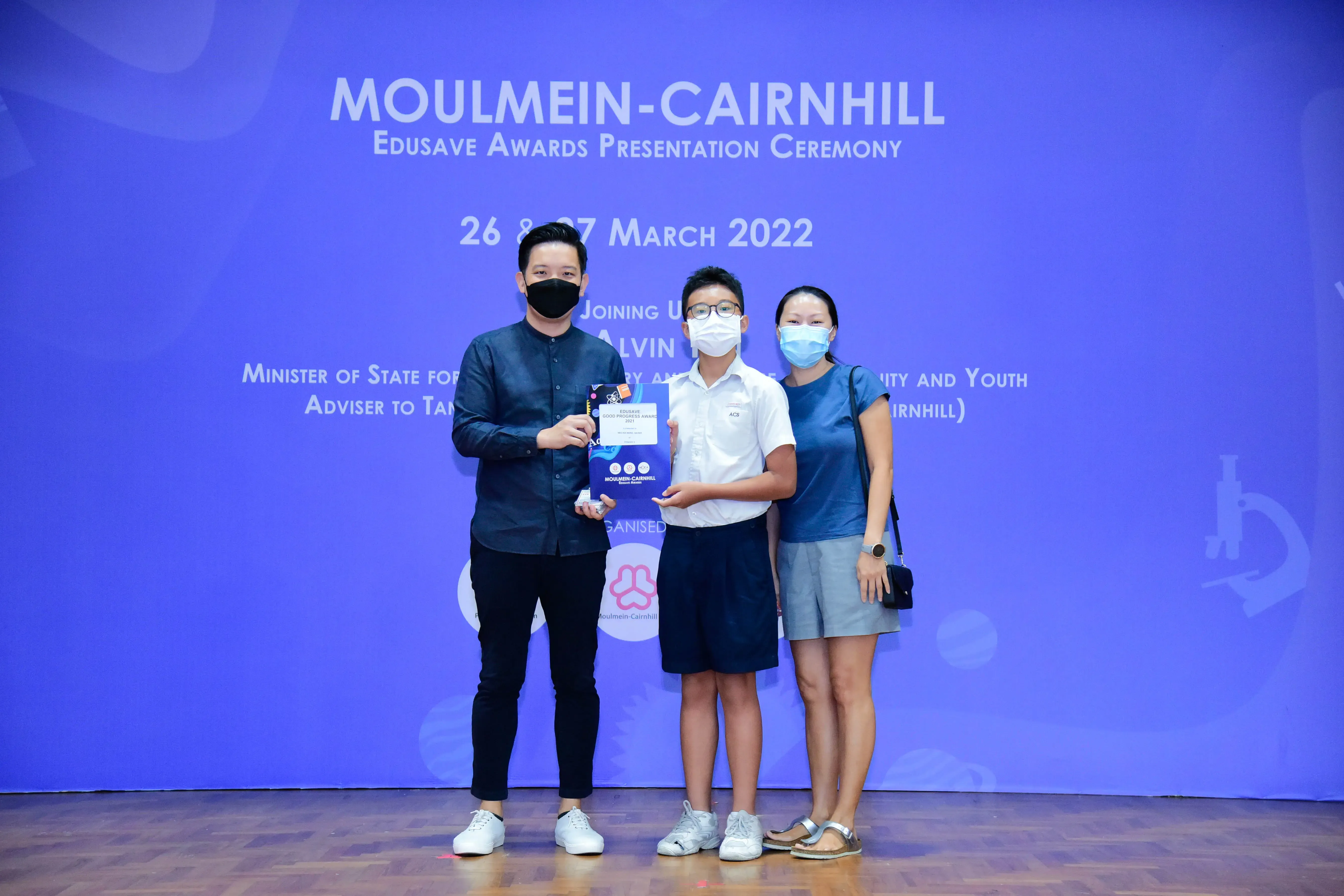 Three masked people pose with an award at the Moulmein-Cairnhill Edusave Awards Ceremony, March 2022.