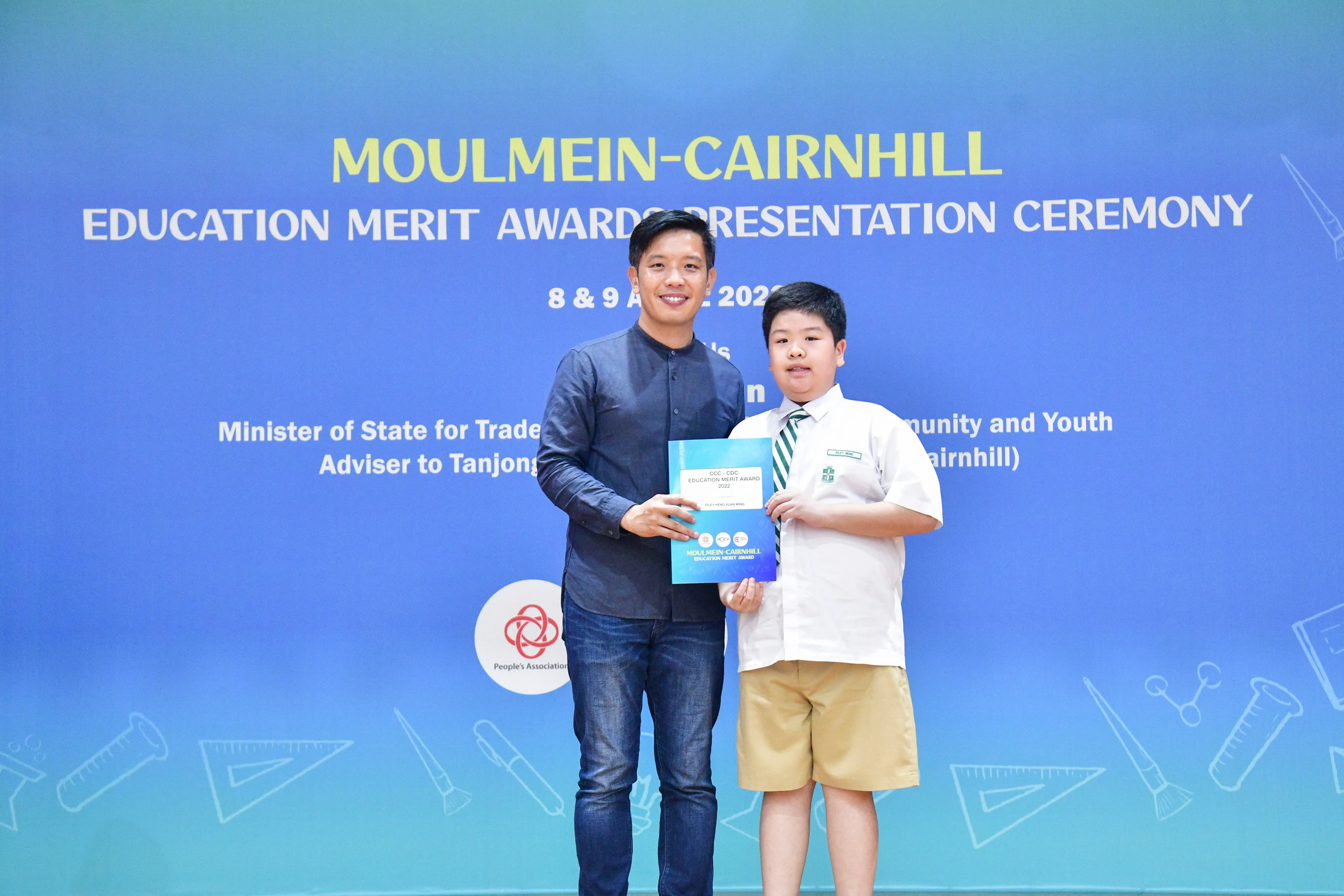 An adult and a young boy hold an award certificate at the Moulmein-Cairnhill Education Merit Awards Presentation Ceremony.