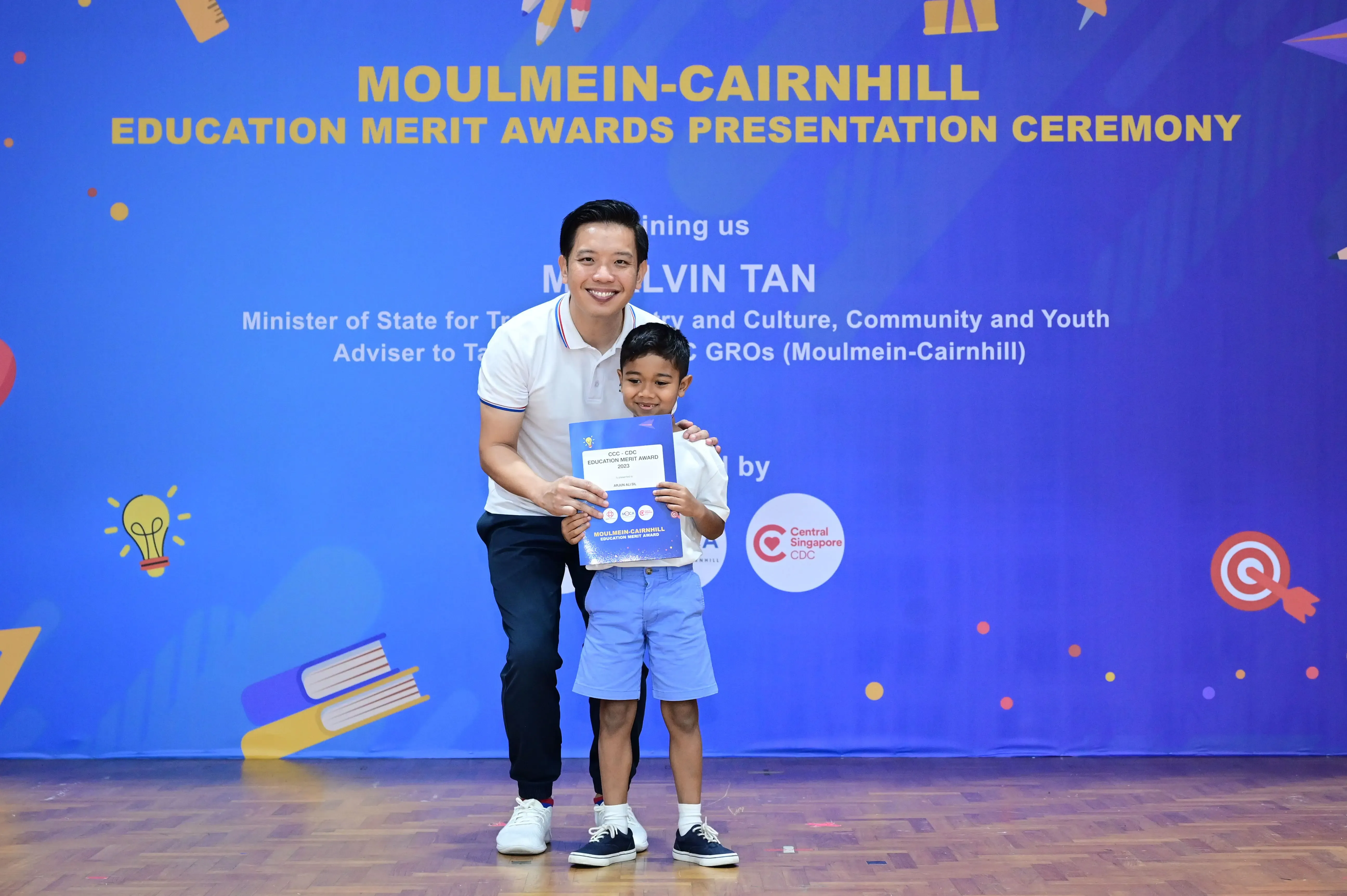 A man and young boy hold a merit award certificate at the Moulmein-Cairnhill Education Merit Awards Ceremony.