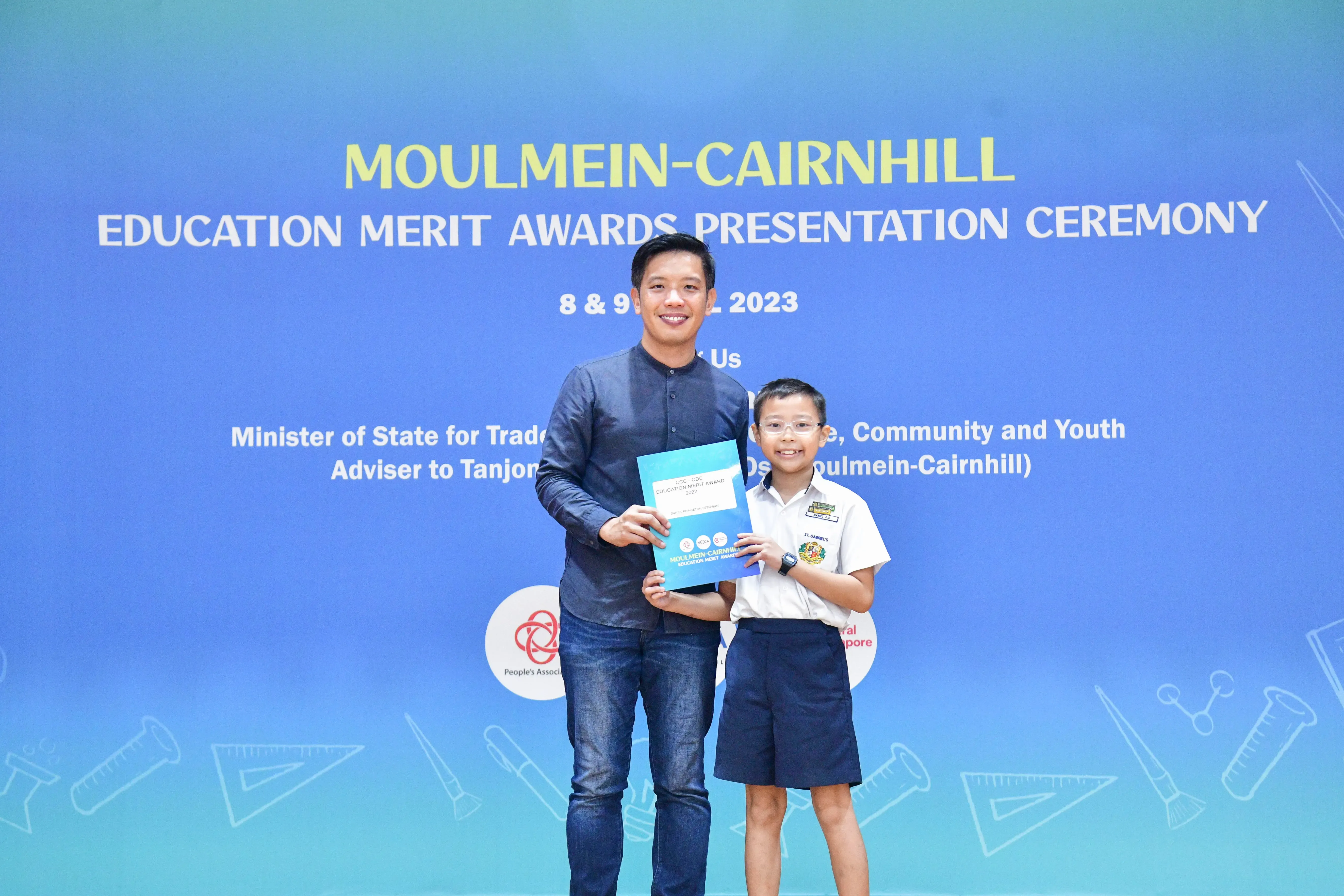 An adult and a young student in school uniform pose together holding an award at the Moulmein-Cairnhill Education Merit Awards 2023.