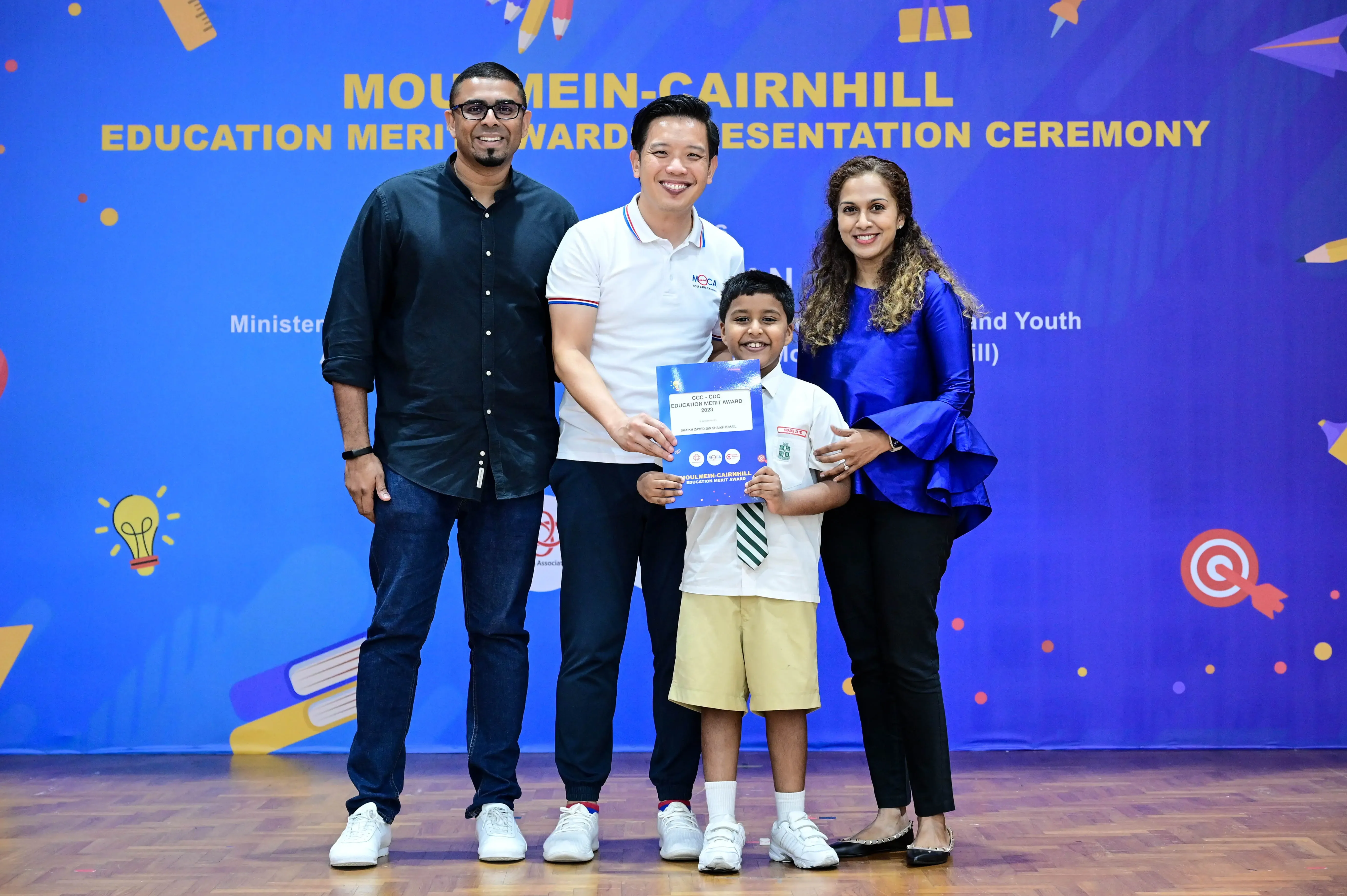 Three adults and a young boy holding an award certificate at the Moulmein-Cairnhill Education Merit Award Ceremony.