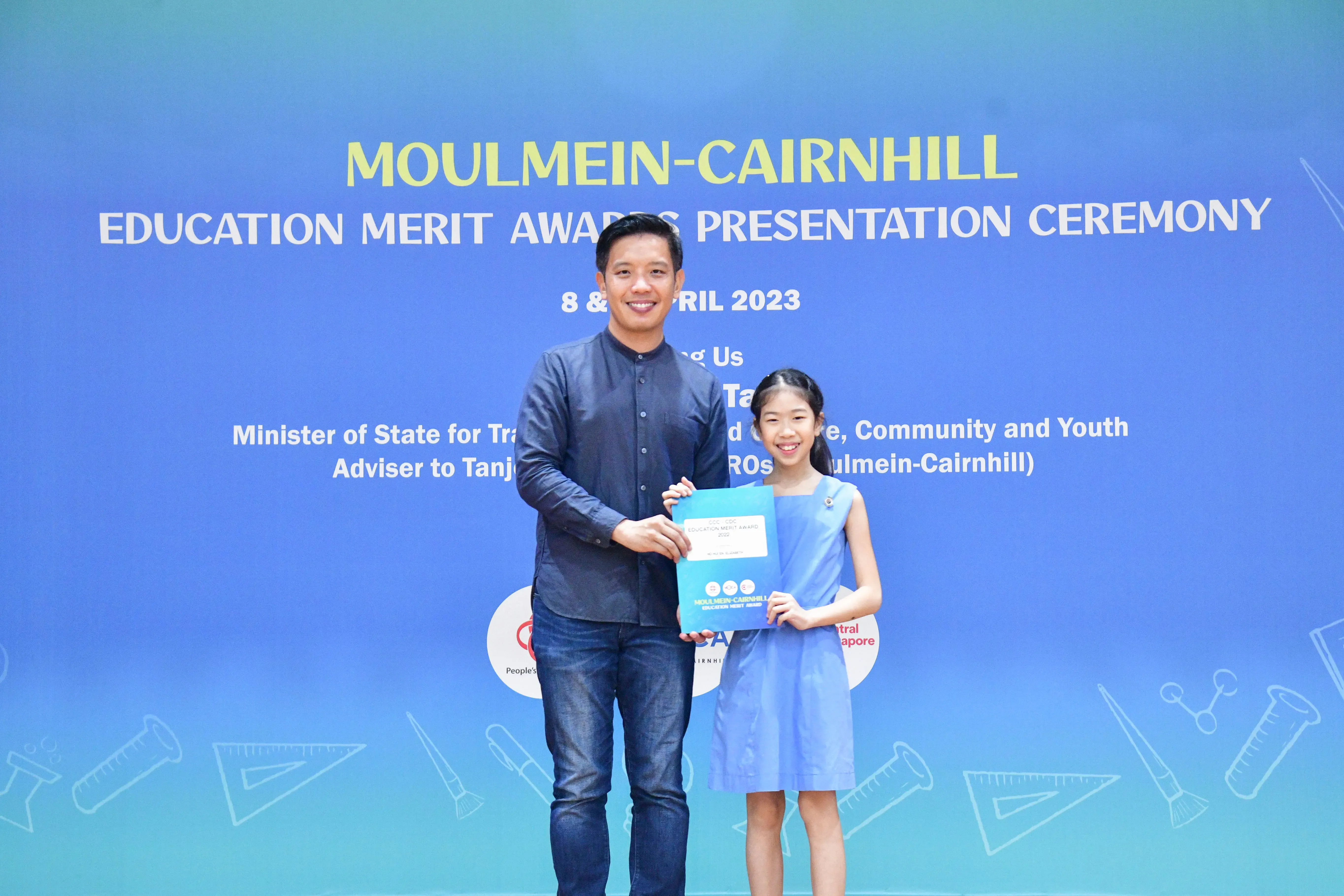 A man and a young girl hold a certificate together at the Moulmein-Cairnhill Education Merit Awards ceremony, April 2023.