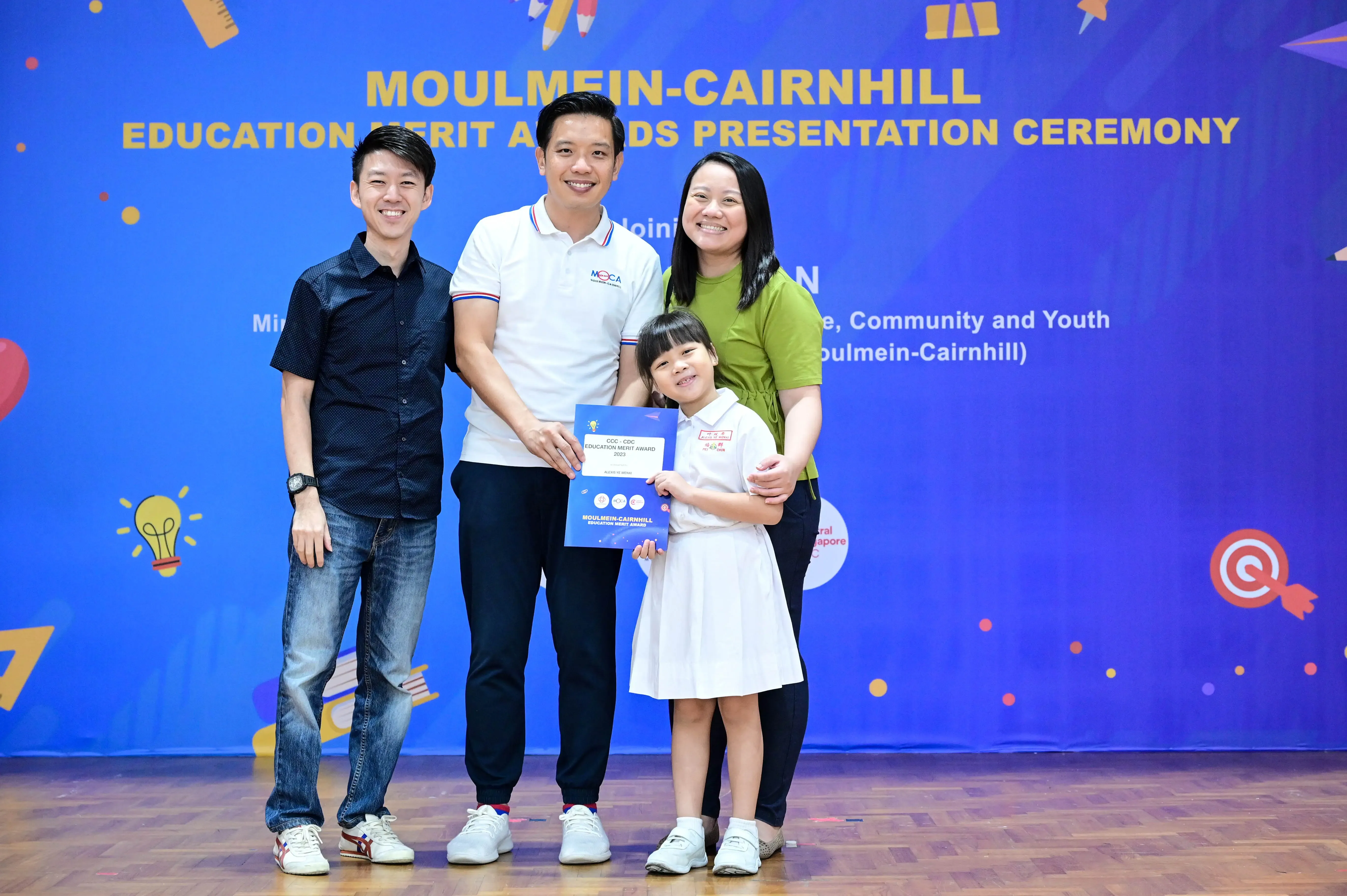 Three adults and a young girl pose with a certificate at the Moulmein-Cairnhill Education Merit Awards ceremony.