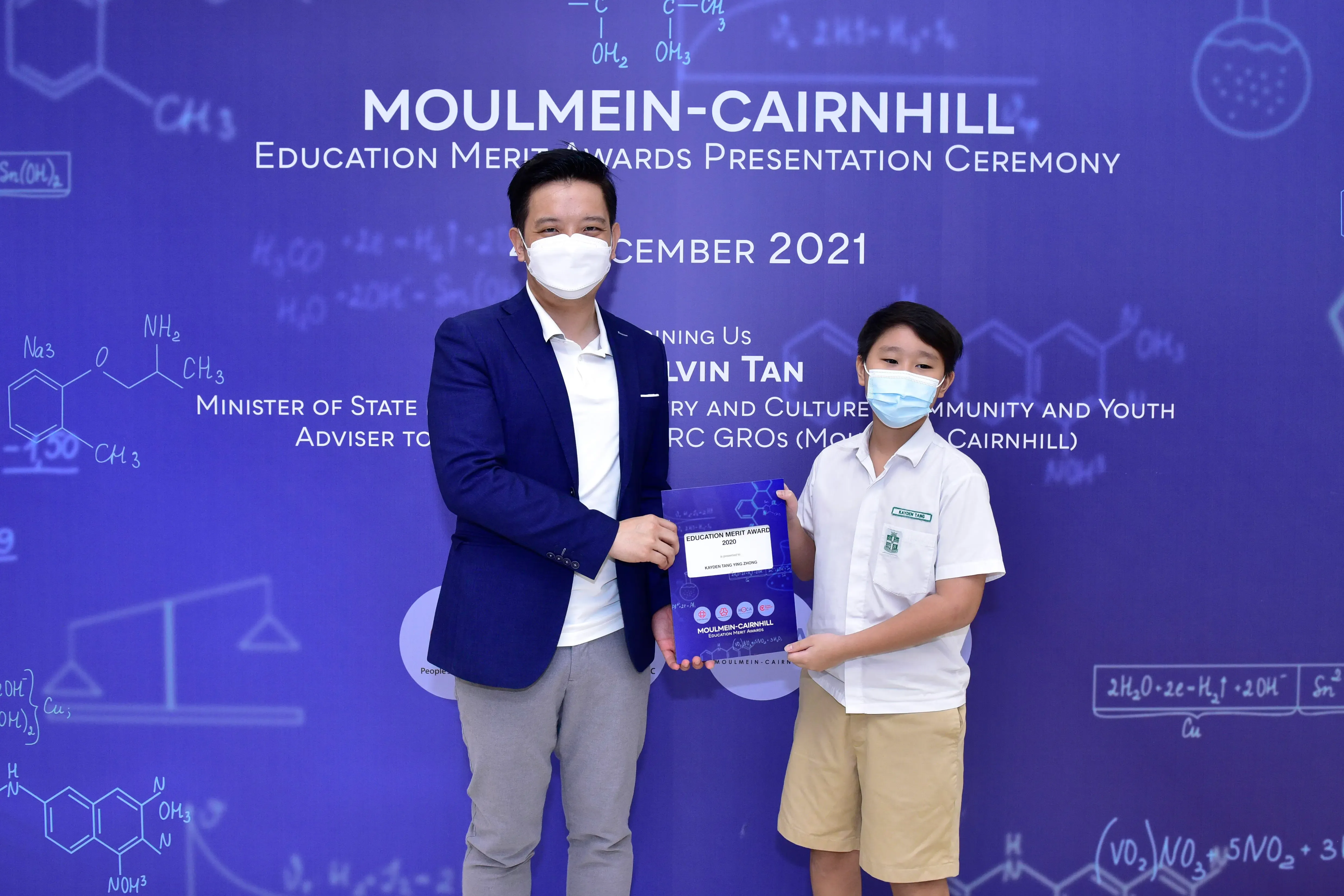 An adult and a young student in masks hold an award certificate at the Moulmein-Cairnhill Education Merit Awards 2021.