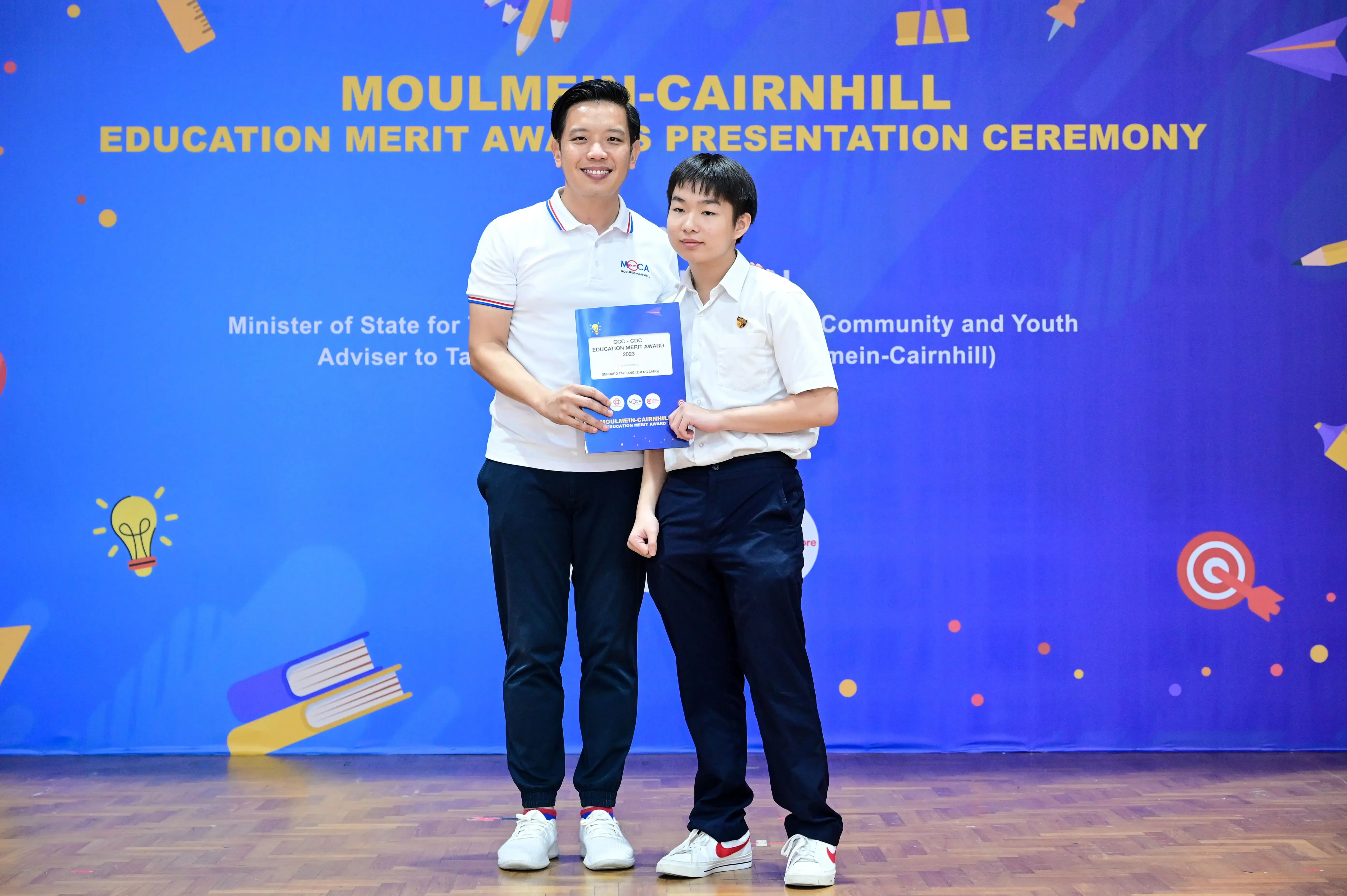 Two people pose holding an award booklet at the Moulmein-Cairnhill Education Merit Award Presentation Ceremony.