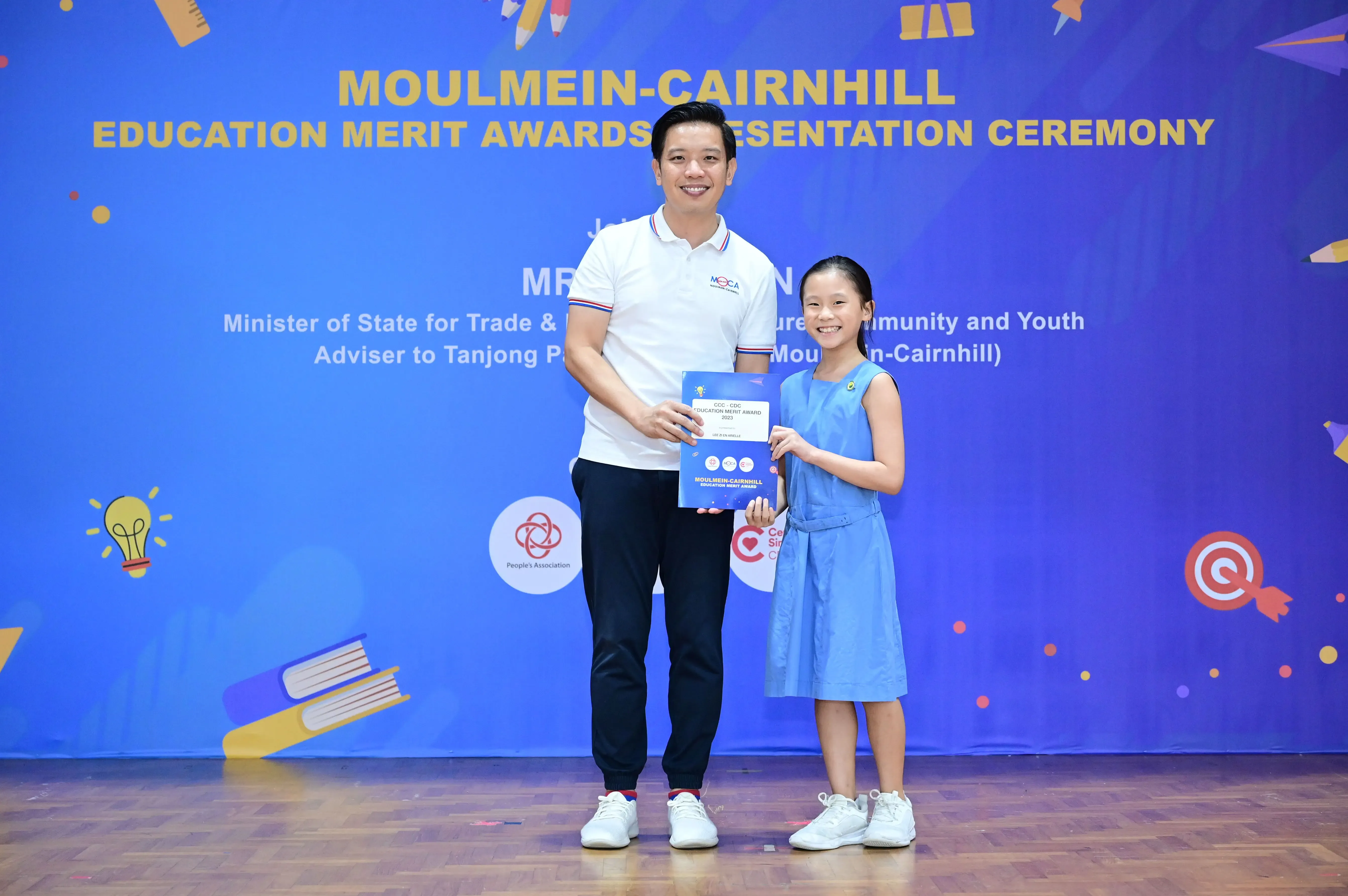 A man and a young girl hold an award certificate at the Moulmein-Cairnhill Education Merit Awards Presentation Ceremony.