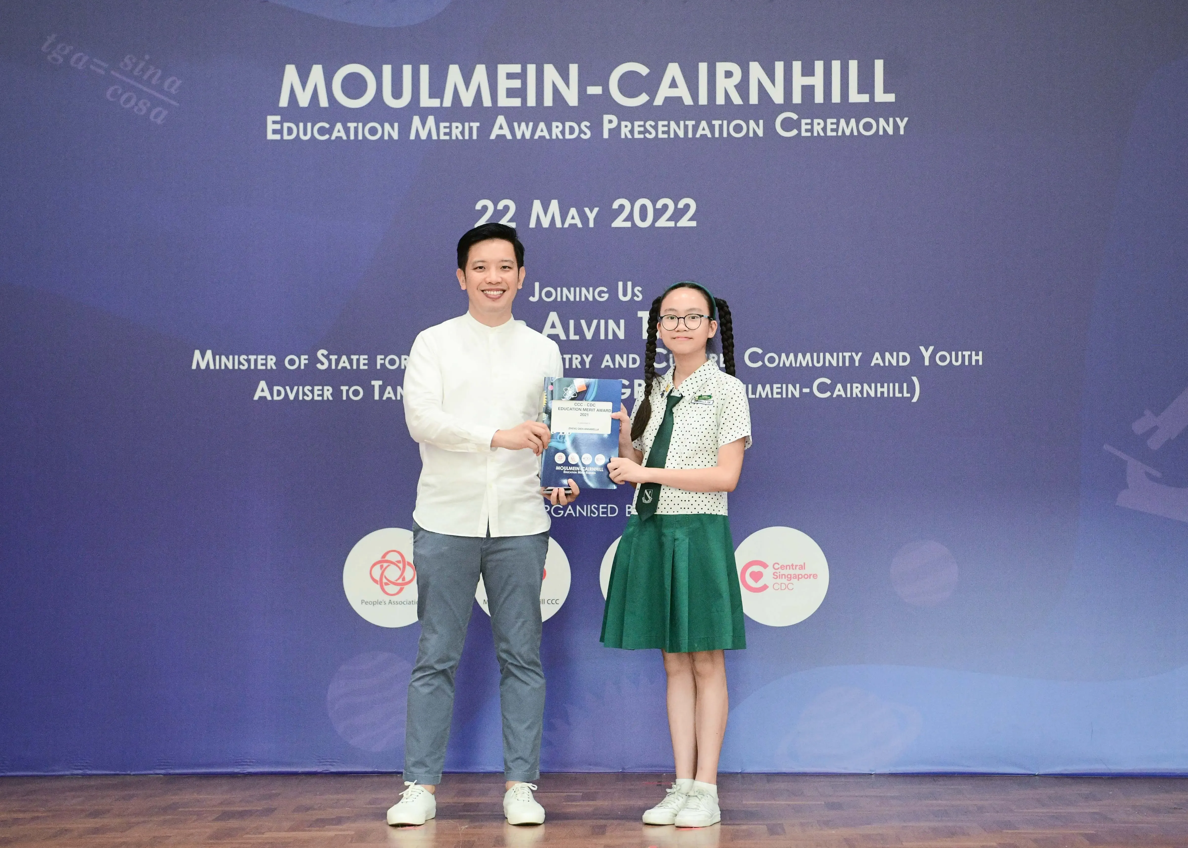 A man and a young girl in school uniform hold an award booklet at the Moulmein-Cairnhill Education Merit Awards ceremony.