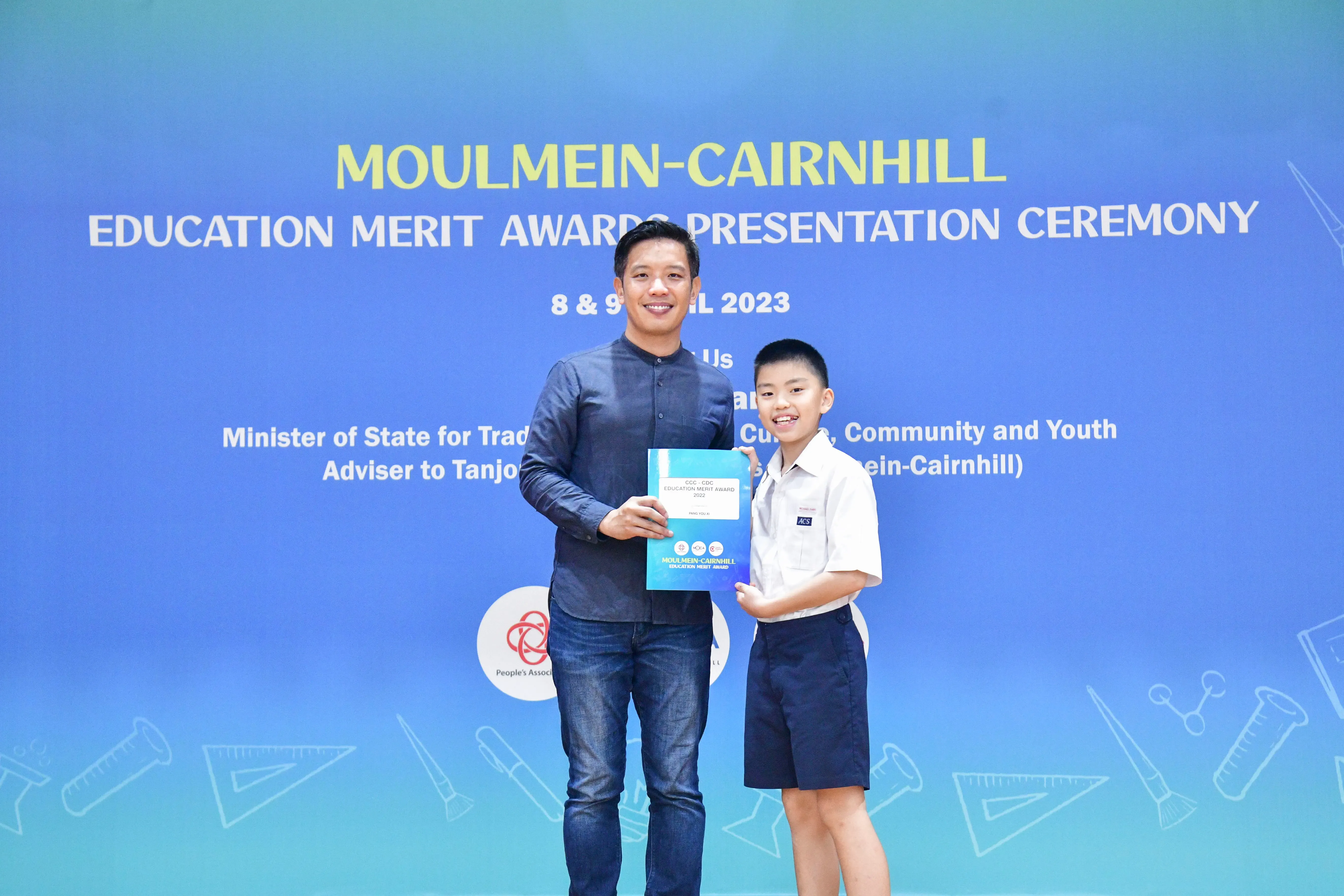 A man and a young boy in school uniform pose holding an award at the Moulmein-Cairnhill Education Merit Awards 2023.