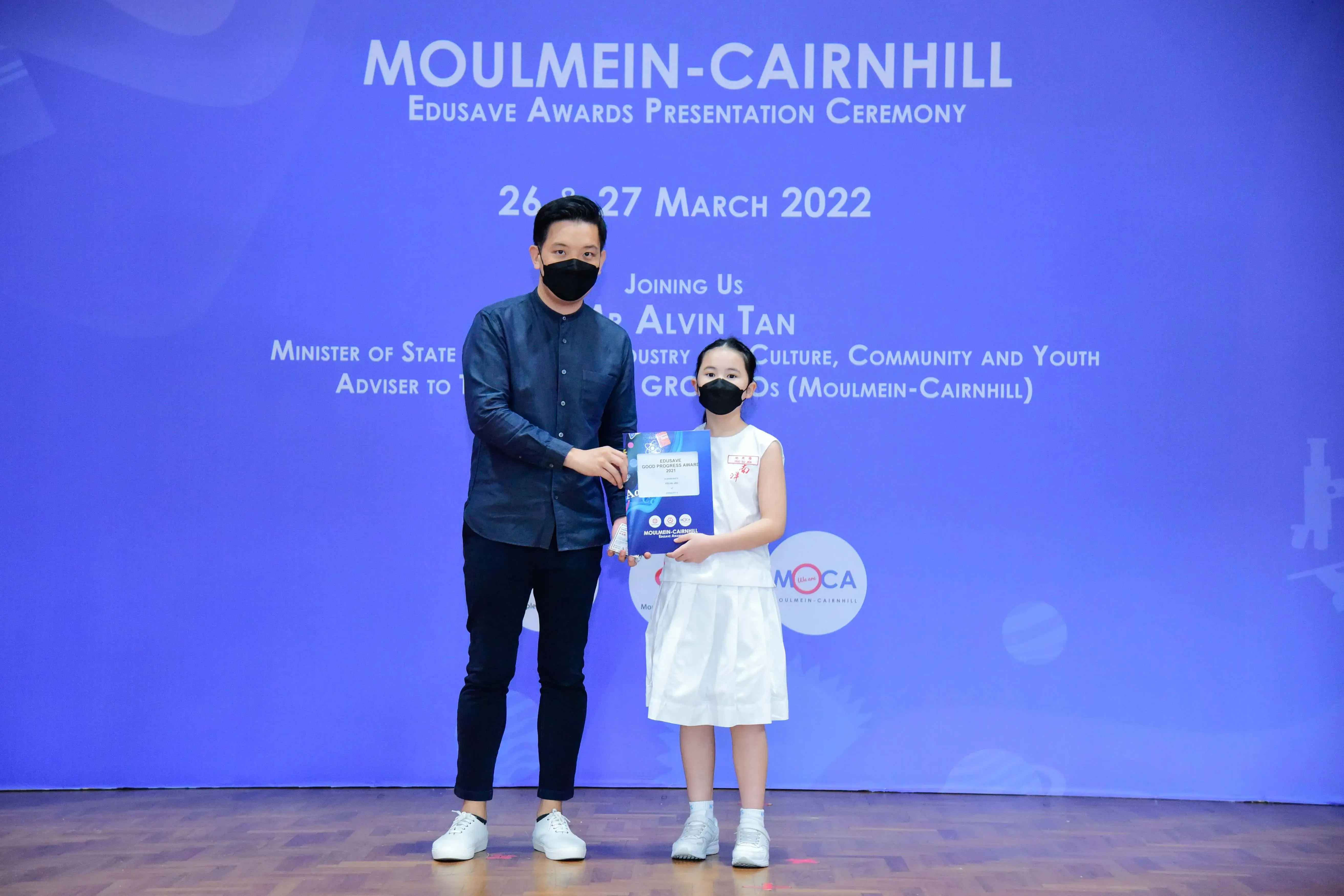 A masked man and young girl hold an award folder at the Moulmein-Cairnhill Edusave Awards Ceremony, March 2022.