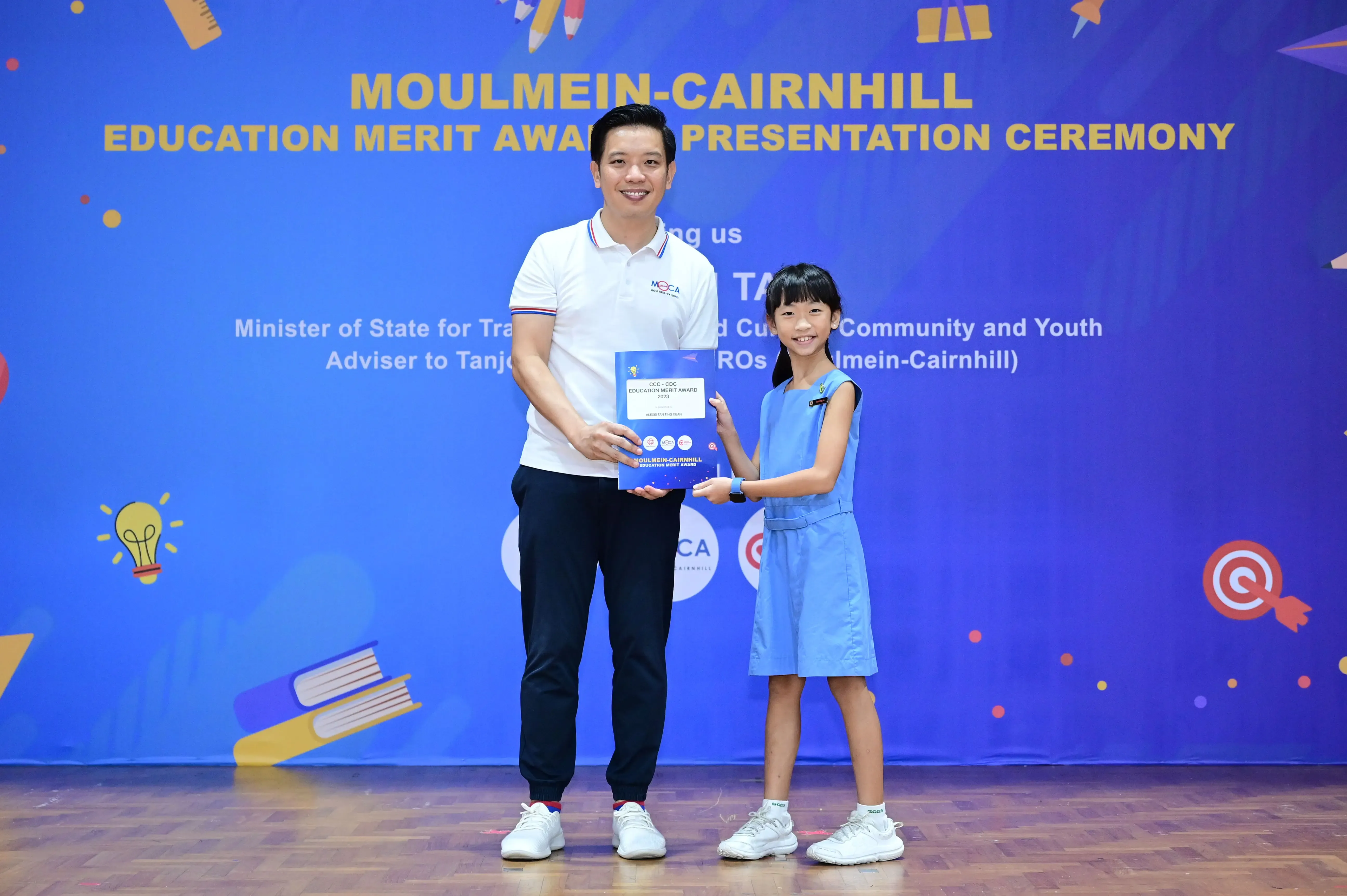 A man and a young girl hold a certificate together at the Moulmein-Cairnhill Education Merit Award Presentation Ceremony.