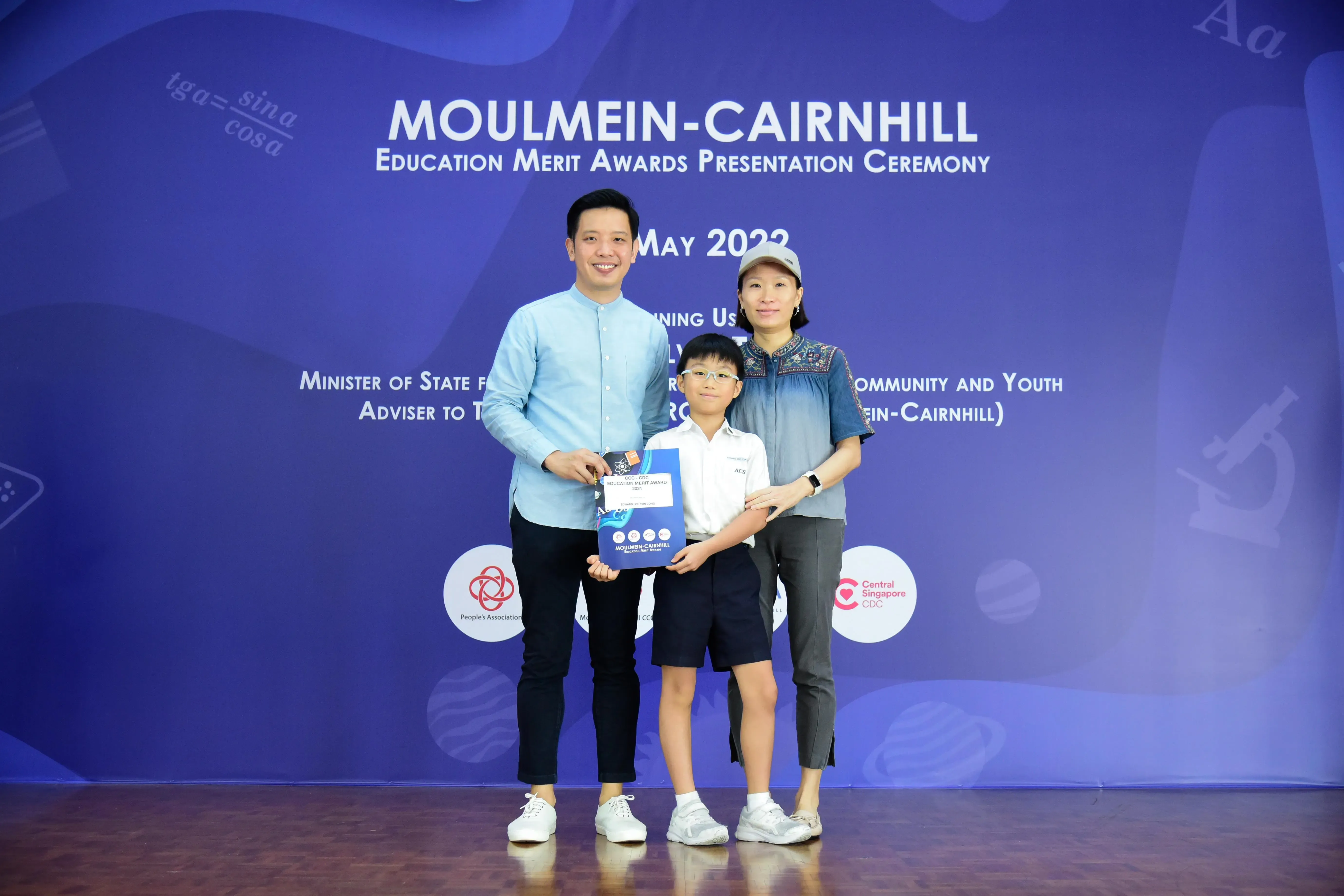 Two adults and a young boy holding an award certificate at the Moulmein-Cairnhill Education Merit Awards 2022.