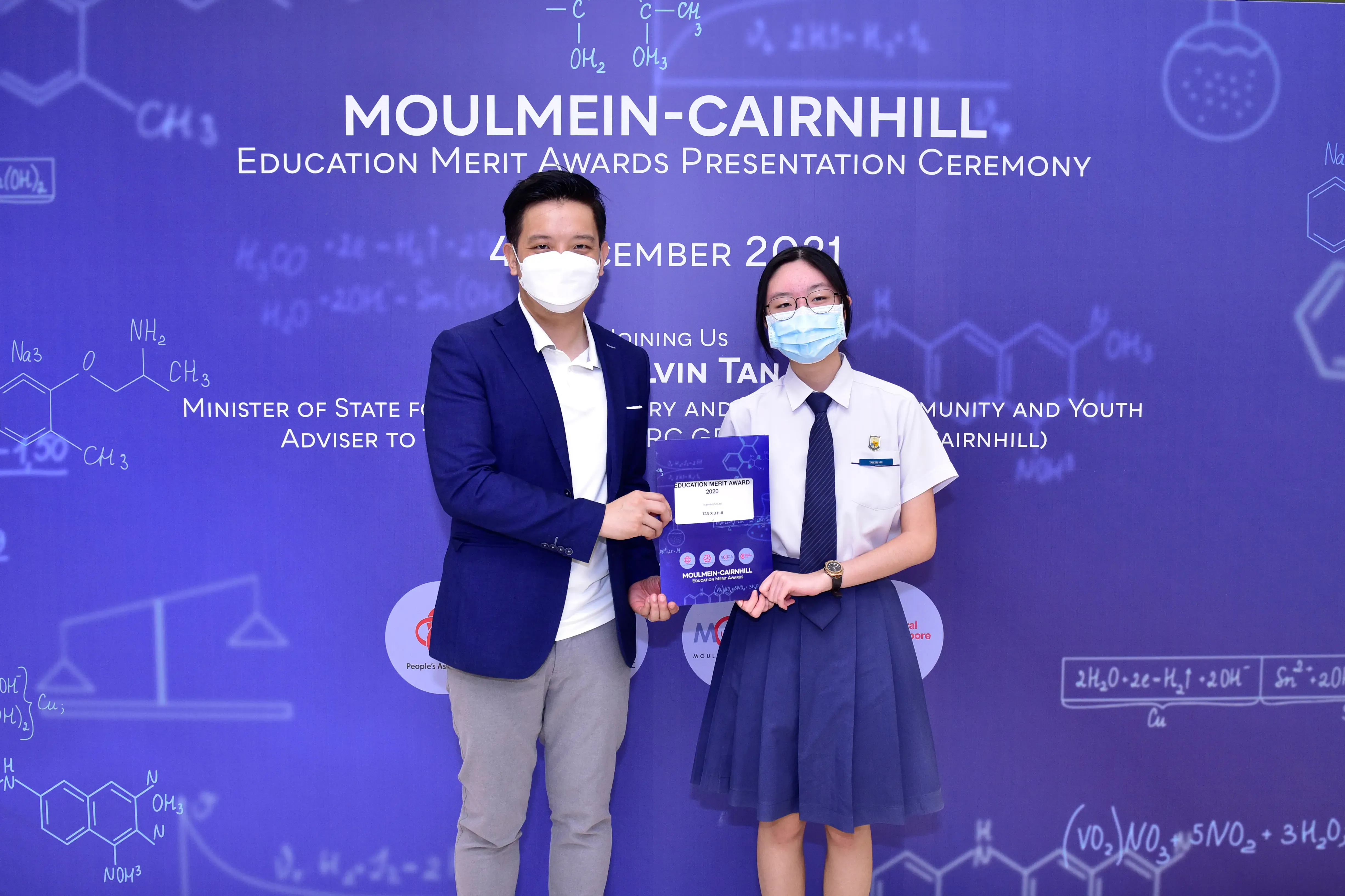 Two masked people hold an award at the Moulmein-Cairnhill Education Merit Awards Presentation Ceremony 2021.