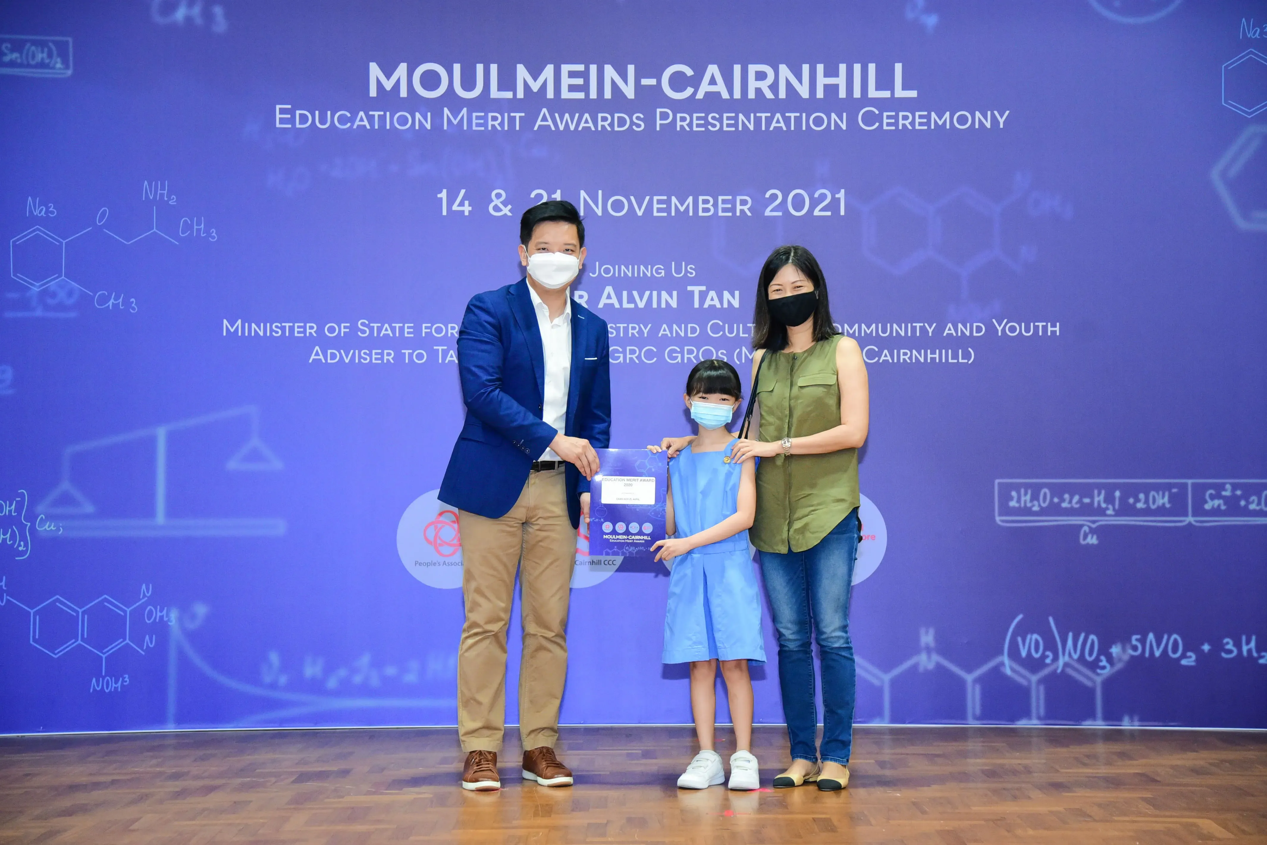 Three masked people hold an award at the Moulmein-Cairnhill Education Merit Awards Ceremony, November 2021.