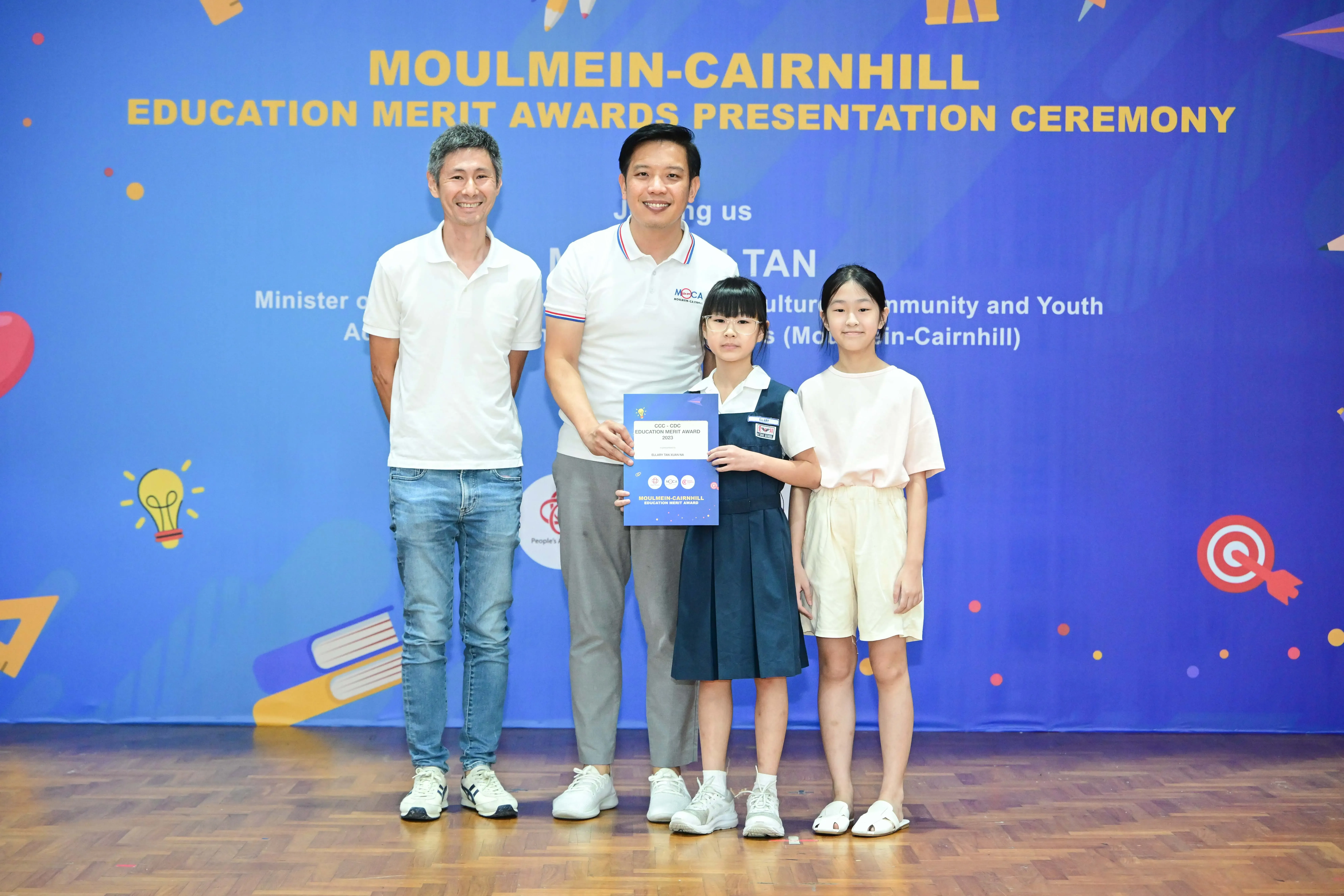 Two men and two girls pose holding an award certificate at the Moulmein-Cairnhill Education Merit Awards Ceremony.