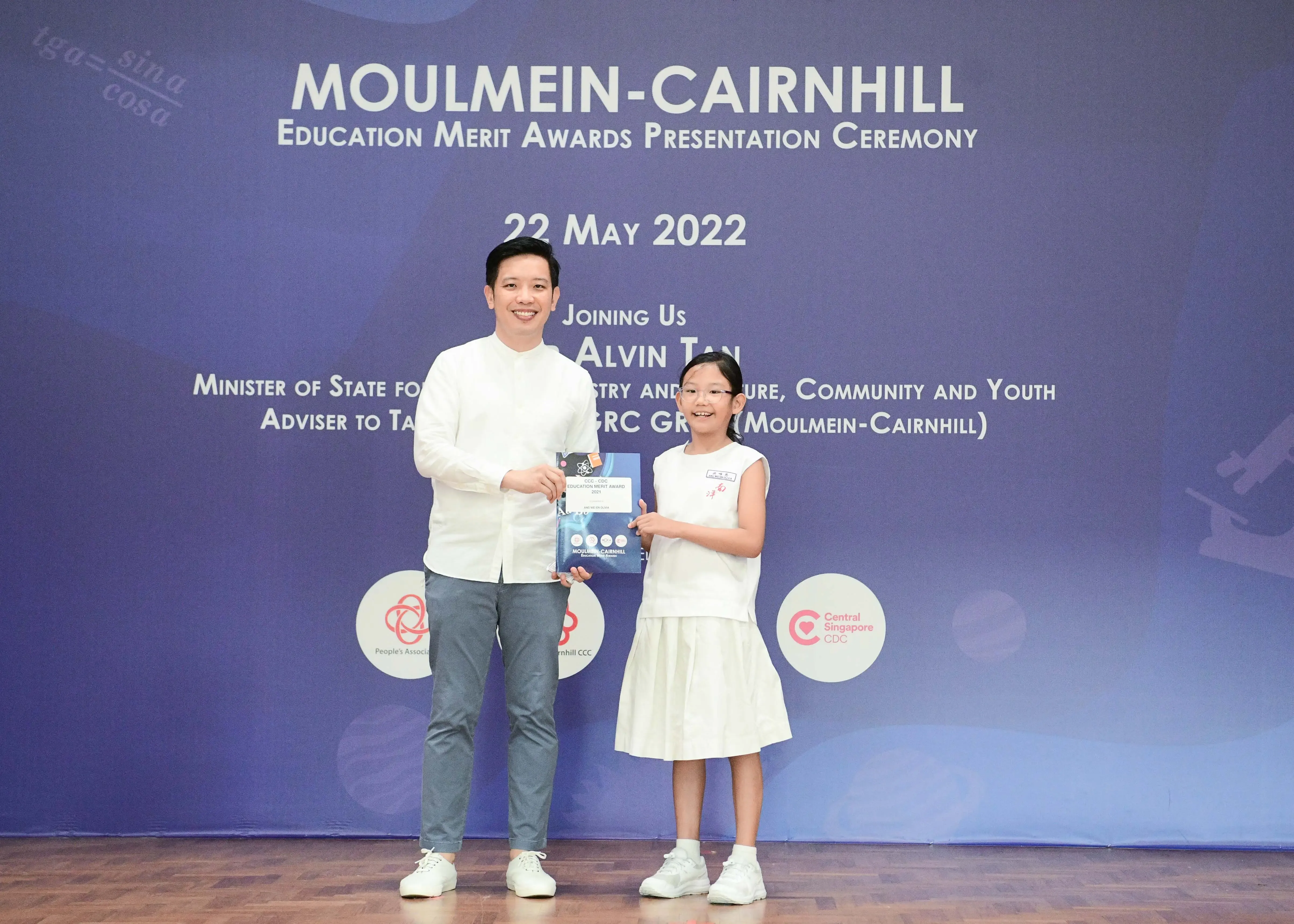 A man and a young girl in white hold an award at the Moulmein-Cairnhill Education Merit Awards on 22 May 2022.